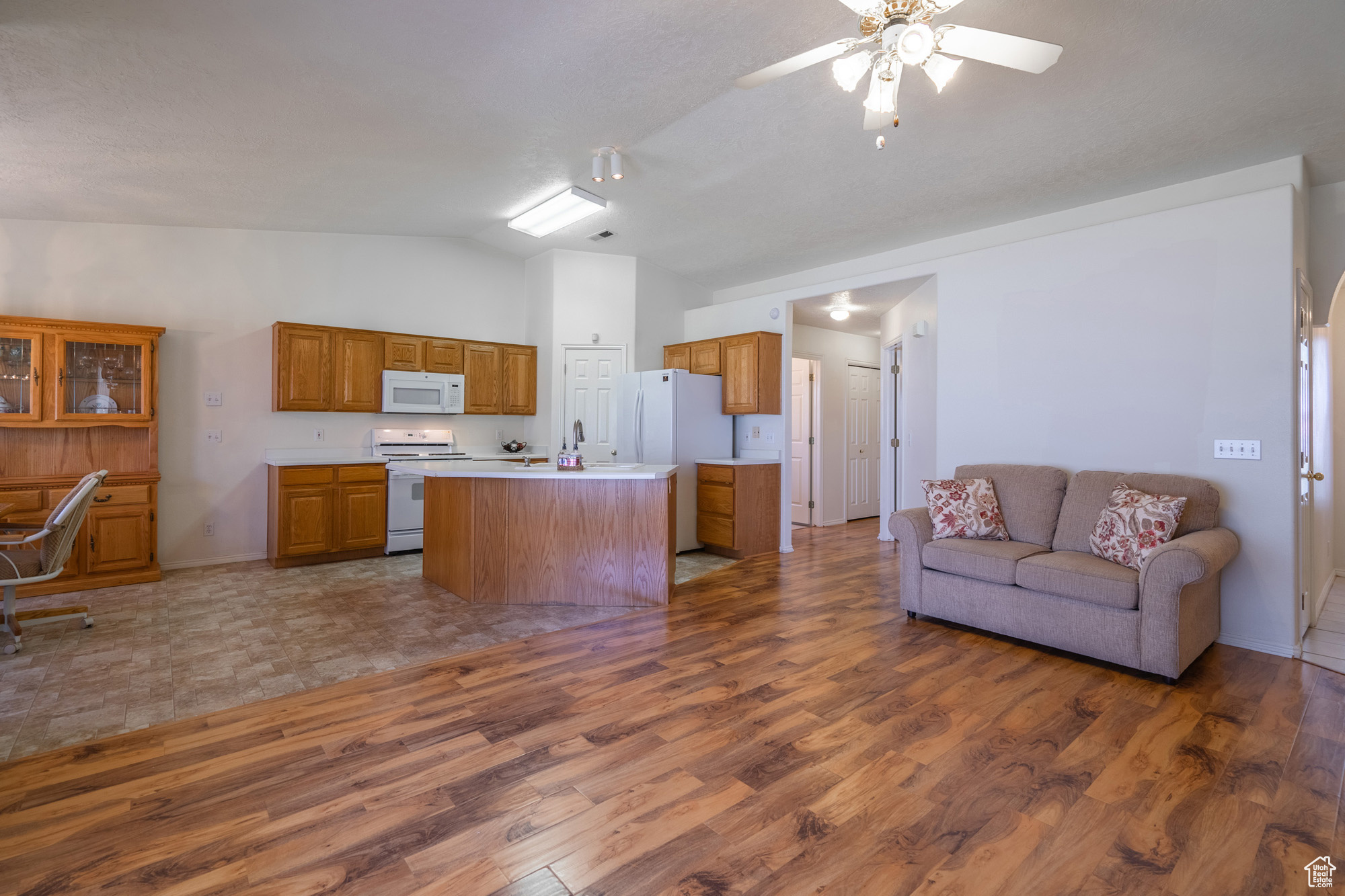 Kitchen vaulted ceiling, white appliances, and an island with sink