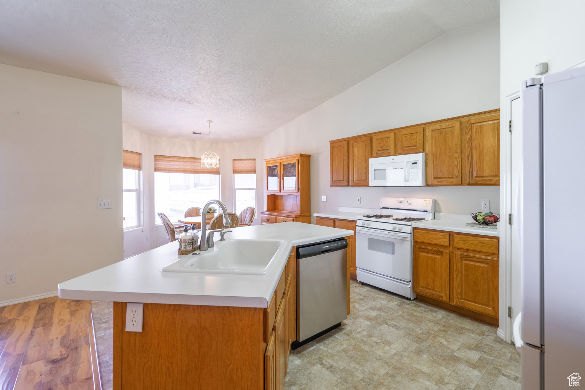 Kitchen with a center island with sink, vaulted ceiling, and white appliances