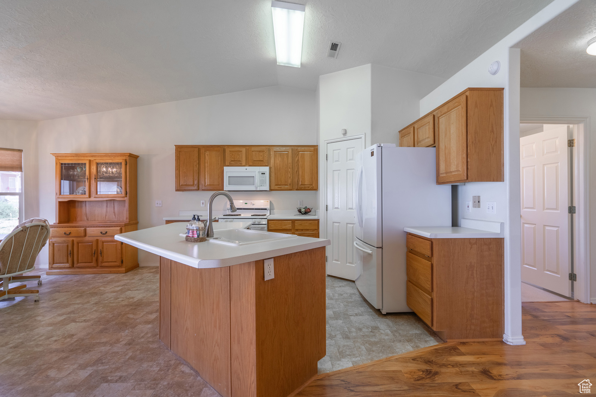 Kitchen with a center island with sink, vaulted ceiling, and white appliances