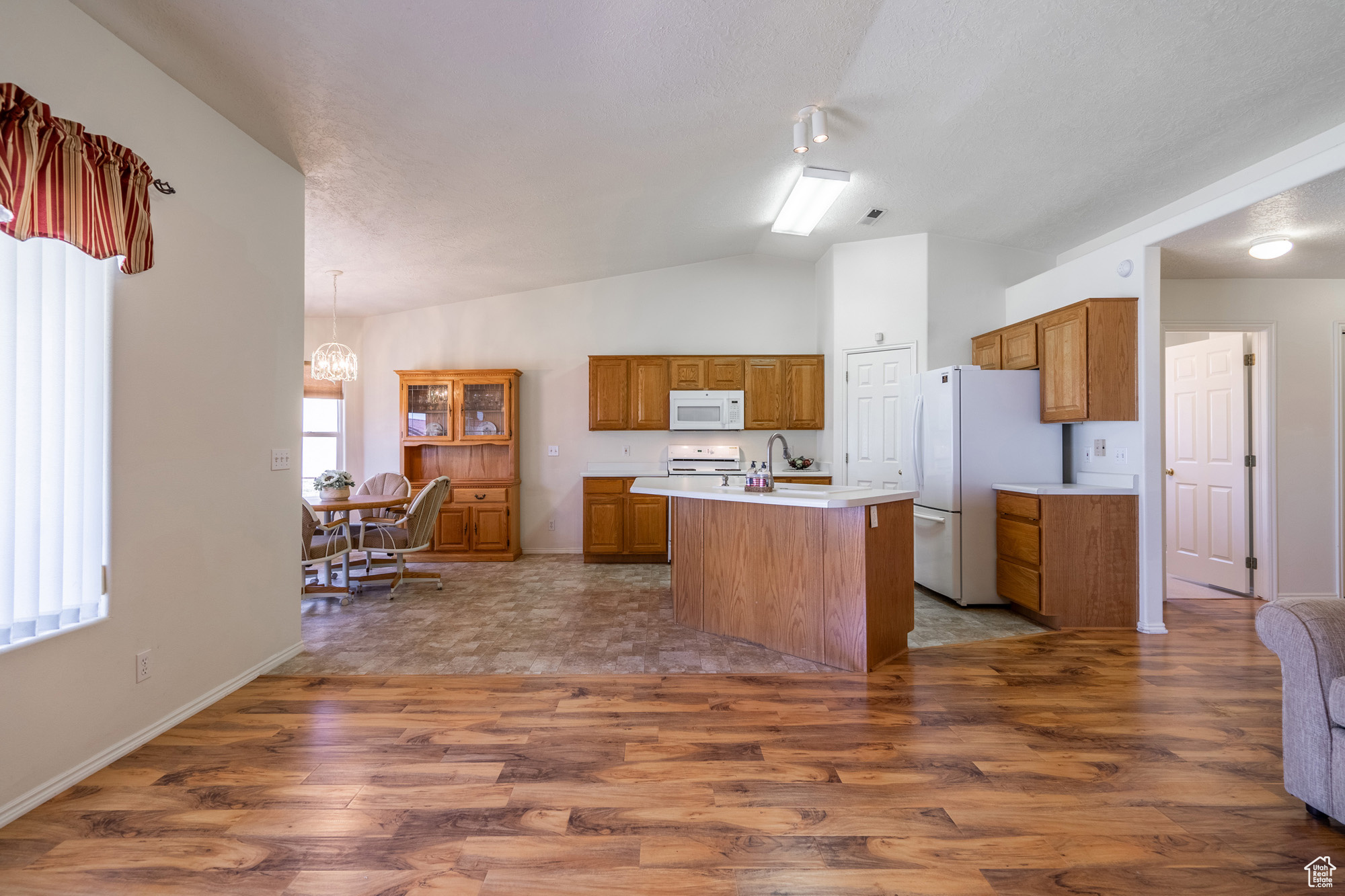 Kitchen featuring a wealth of natural light, an island with sink, and white appliances