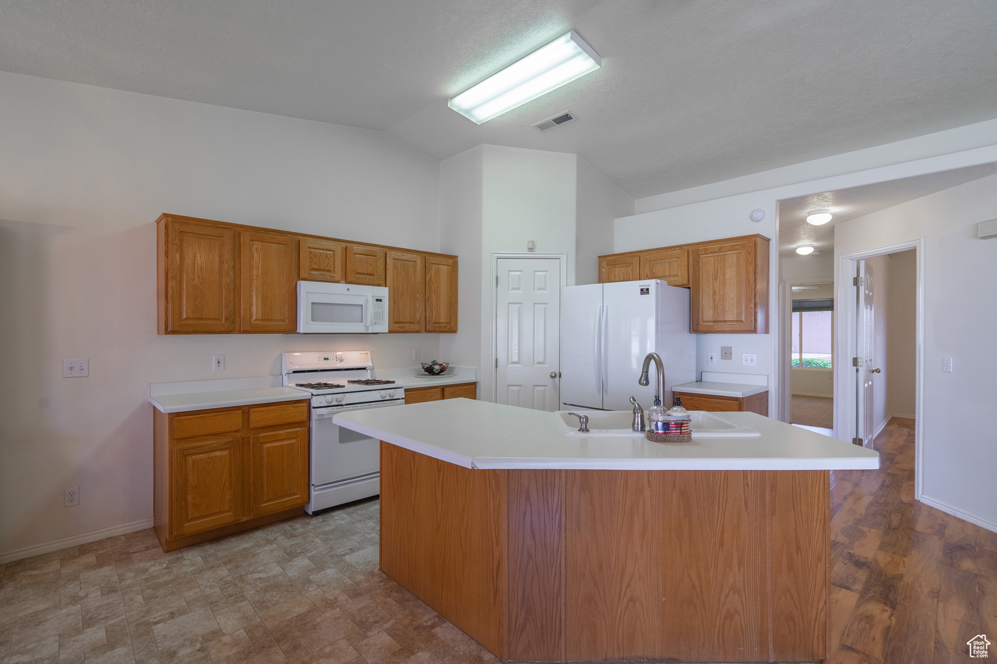 Kitchen with a center island with sink, vaulted ceiling, and white appliances