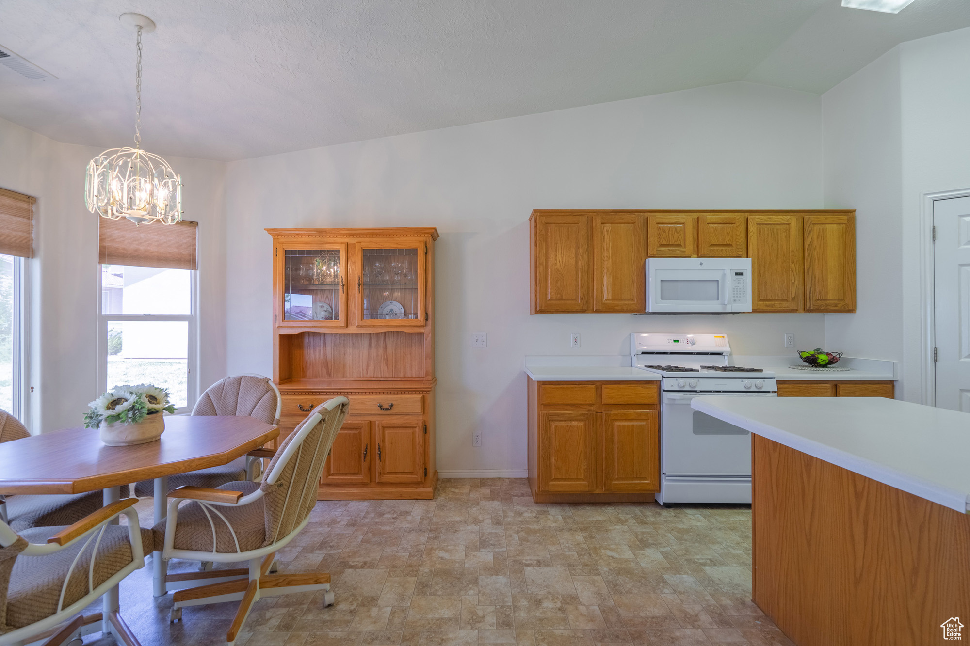 Kitchen with a center island with sink, vaulted ceiling, and white appliances