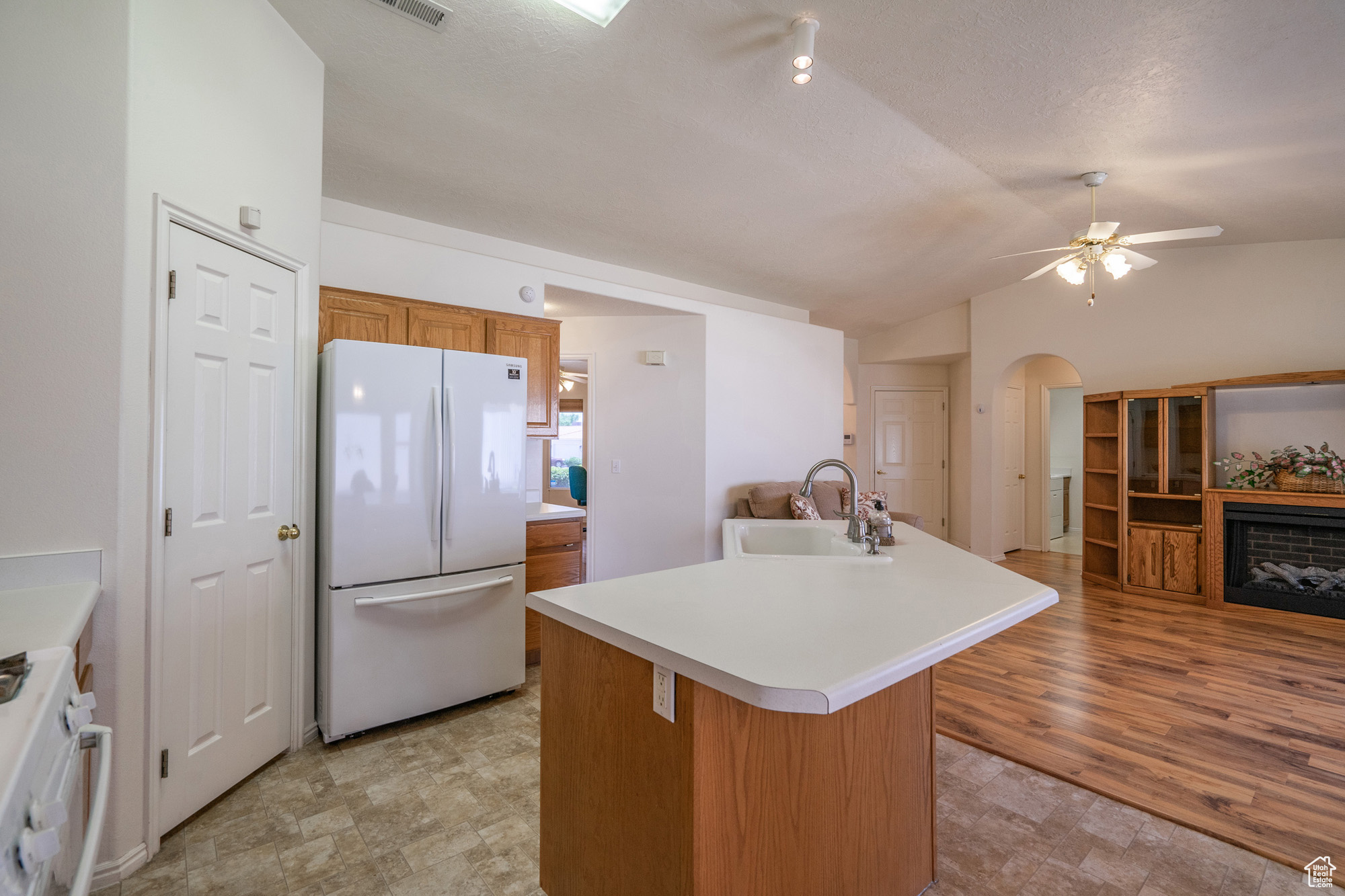 Kitchen featuring white fridge, a fireplace, sink, light hardwood / wood-style flooring, and lofted ceiling