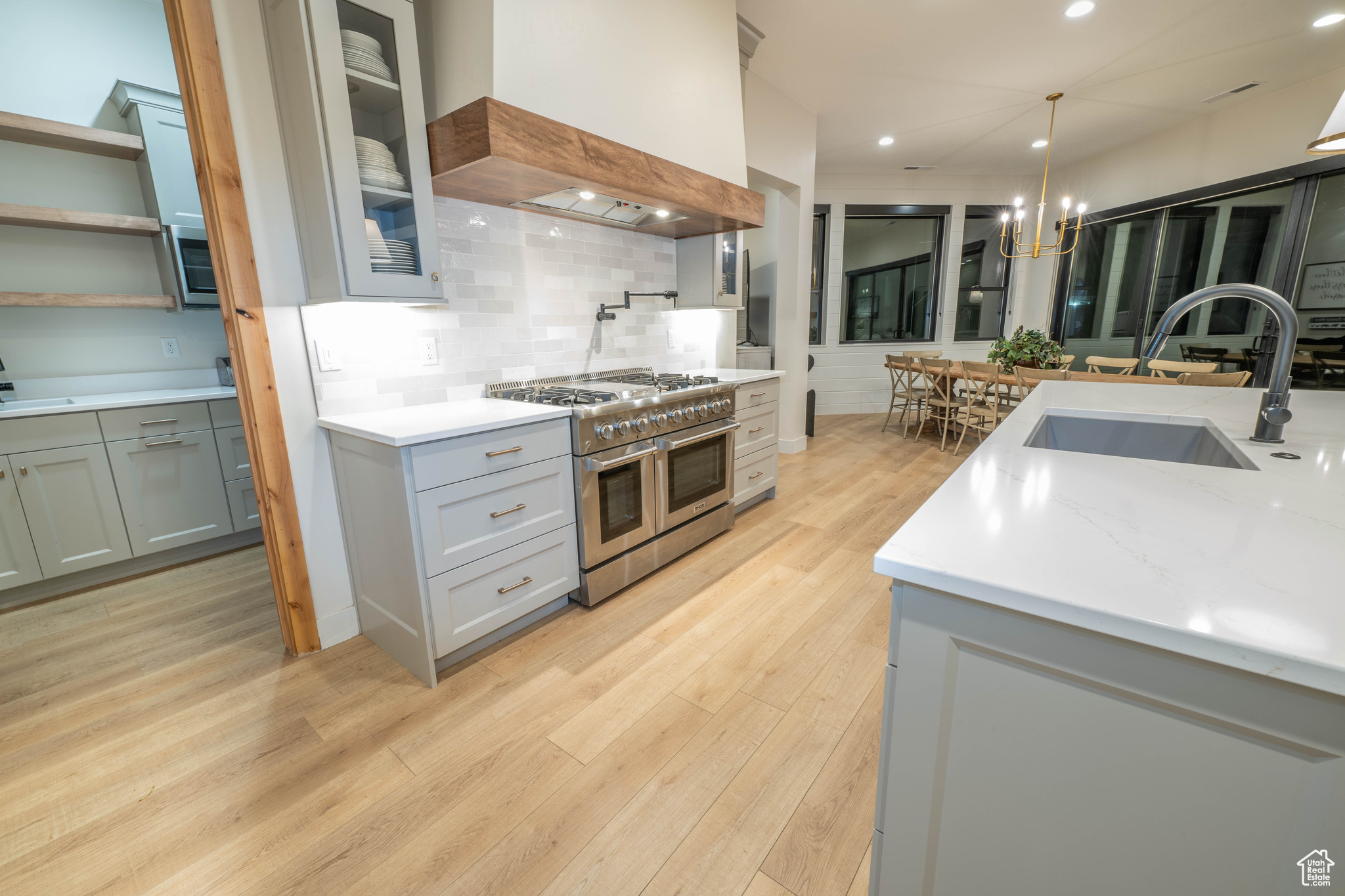 Kitchen featuring light hardwood / wood-style flooring, tasteful backsplash, range with two ovens, custom range hood, and sink