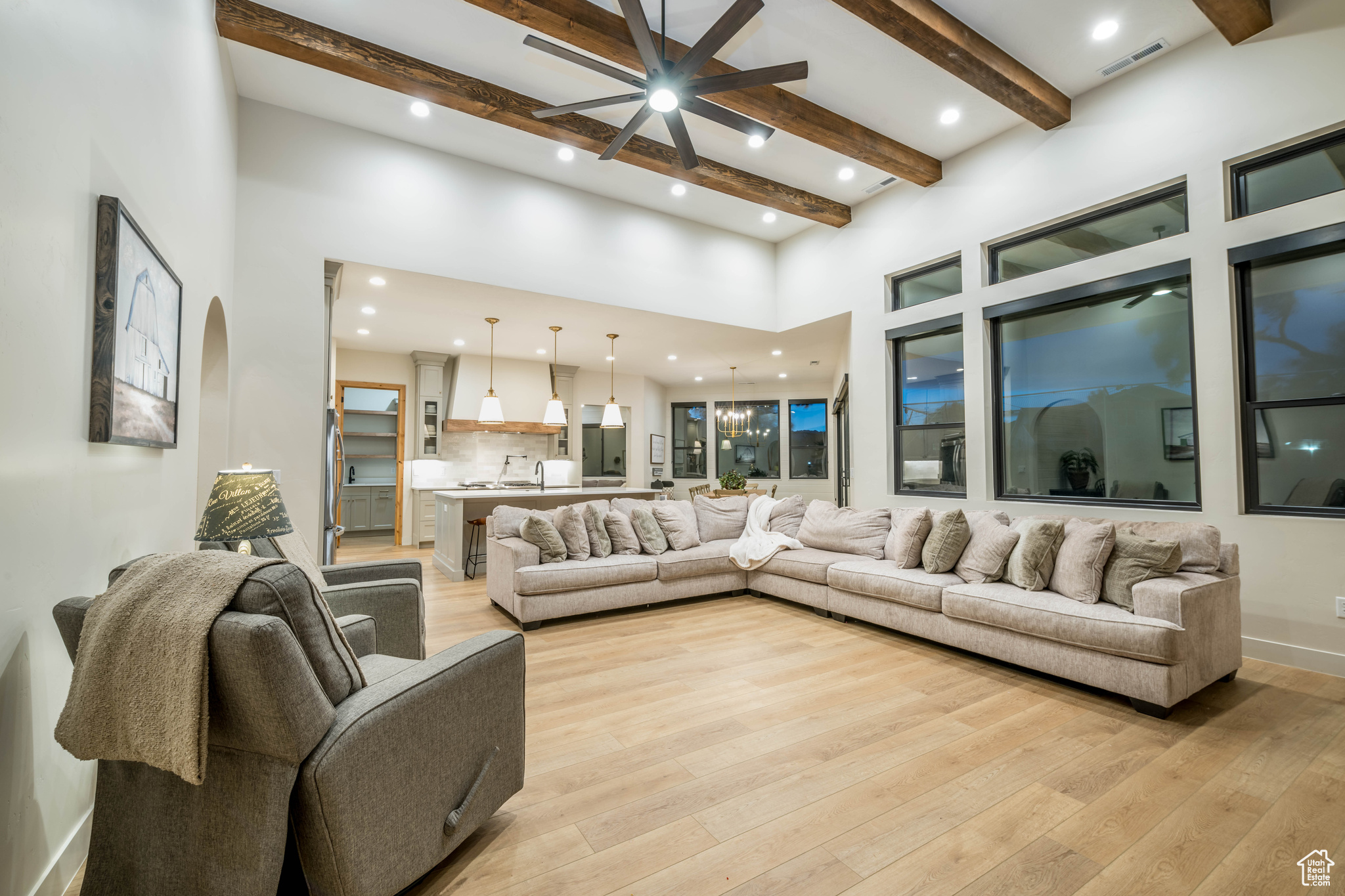 Living room featuring beam ceiling, a high ceiling, ceiling fan, and light wood-type flooring