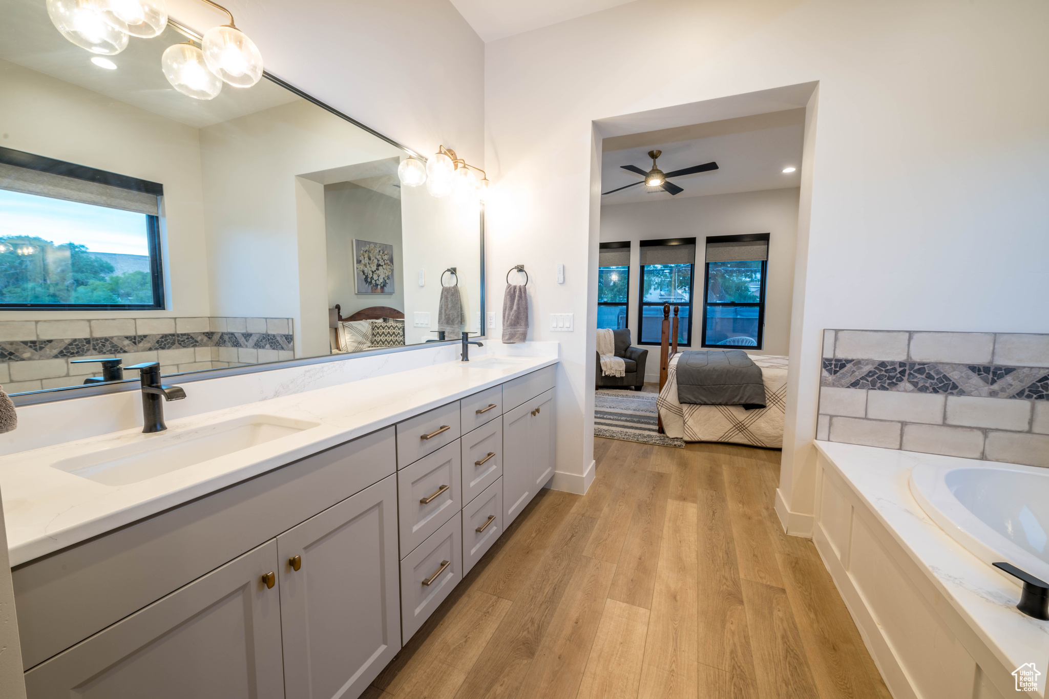 Master Bathroom featuring double sink, a bath to relax in, ceiling fan with notable chandelier, hardwood / wood-style floors, and vanity with extensive cabinet space