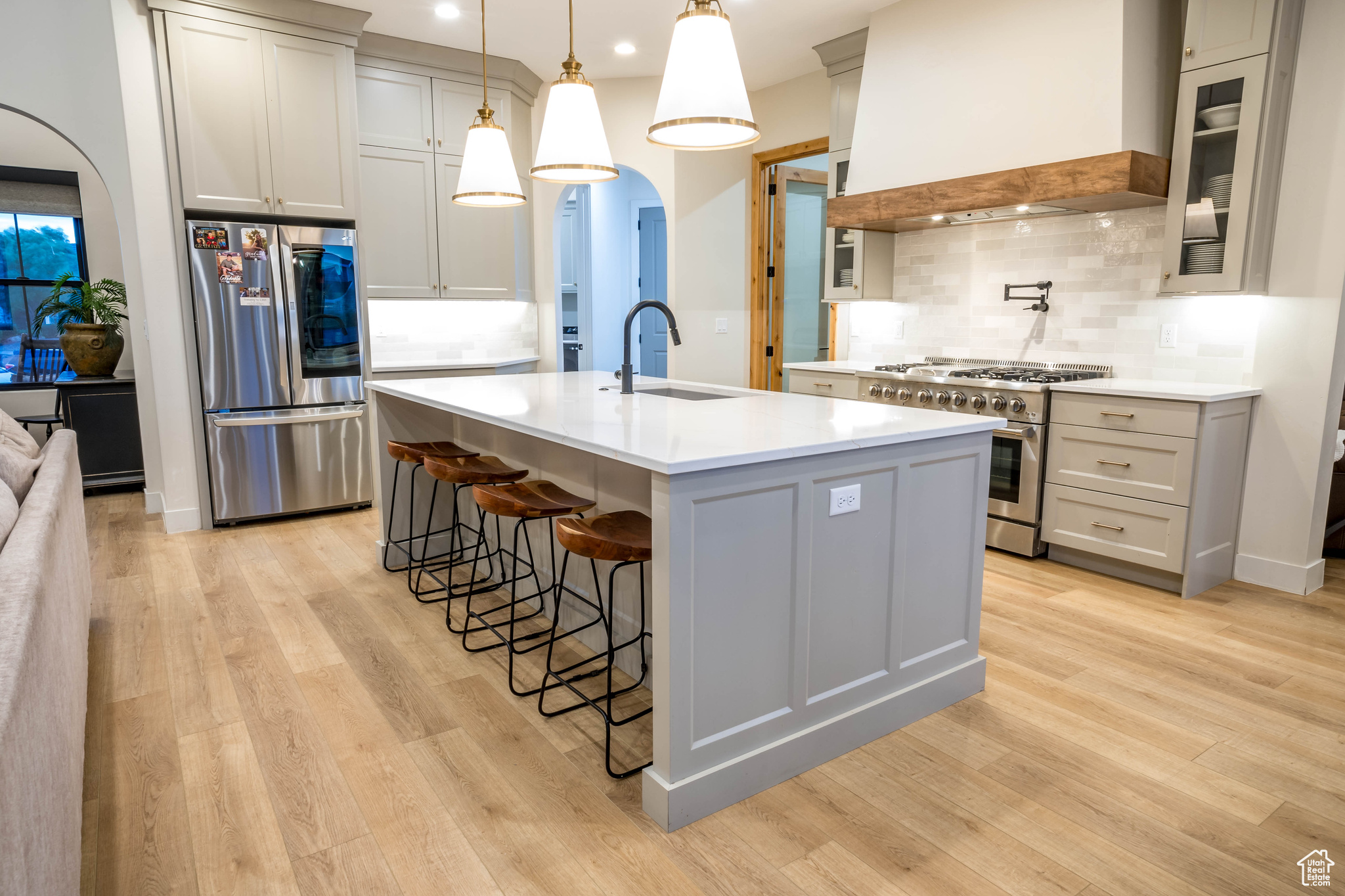 Kitchen featuring tasteful backsplash, a kitchen island with sink, wall chimney exhaust hood, appliances with stainless steel finishes, and sink