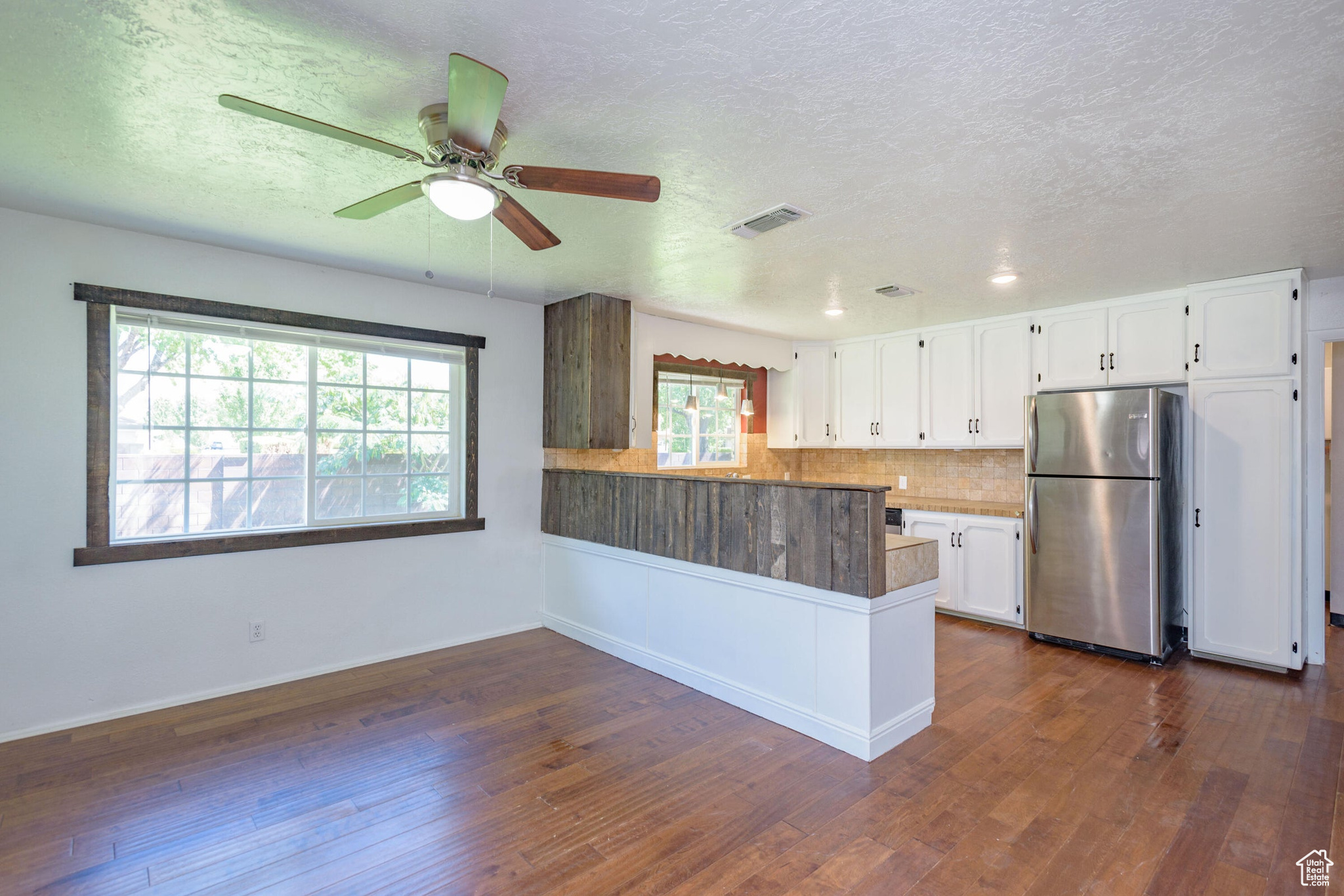 Kitchen with white cabinetry, stainless steel fridge, dark hardwood / wood-style flooring, and kitchen peninsula