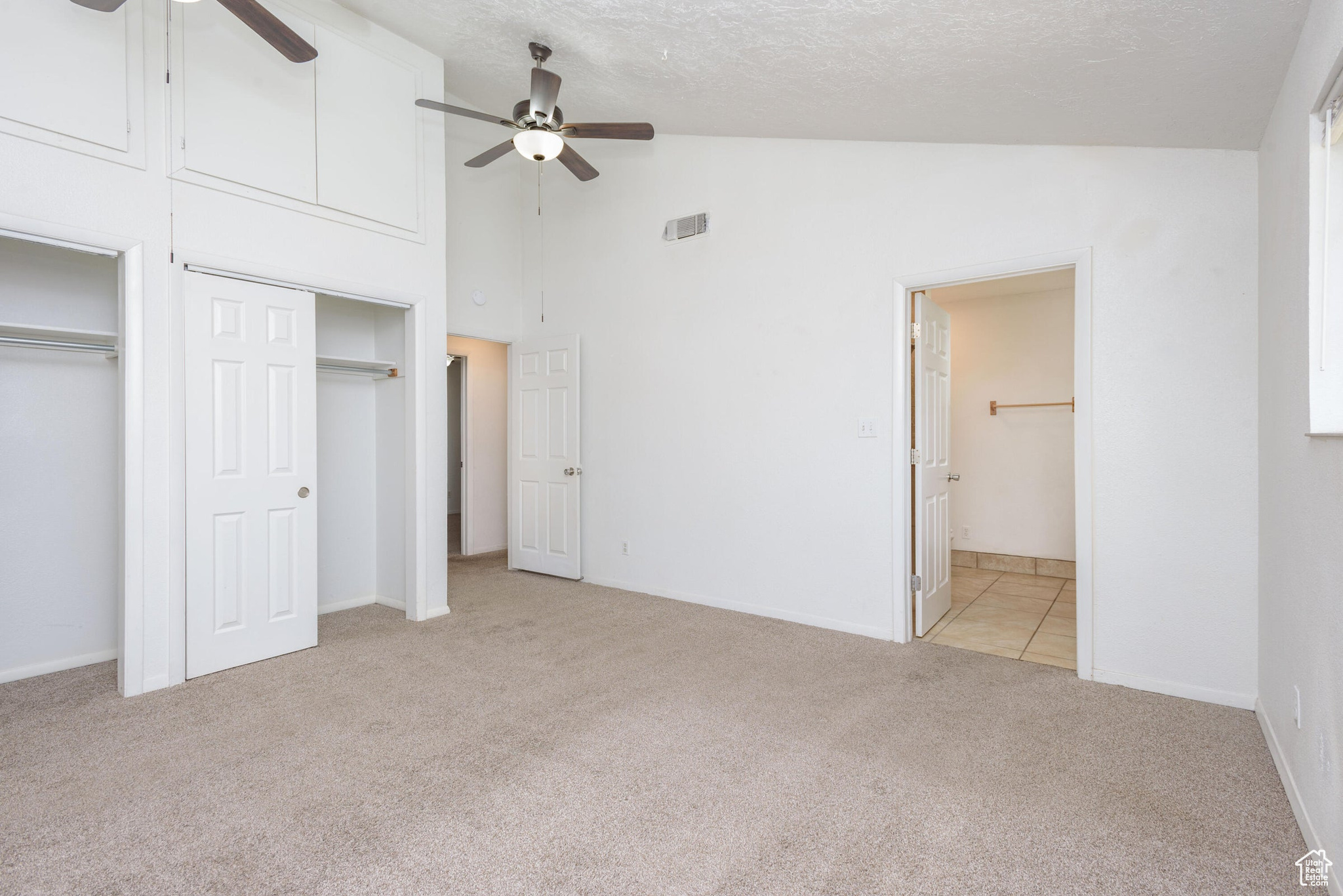 Unfurnished bedroom featuring light carpet, a textured ceiling, and ceiling fan