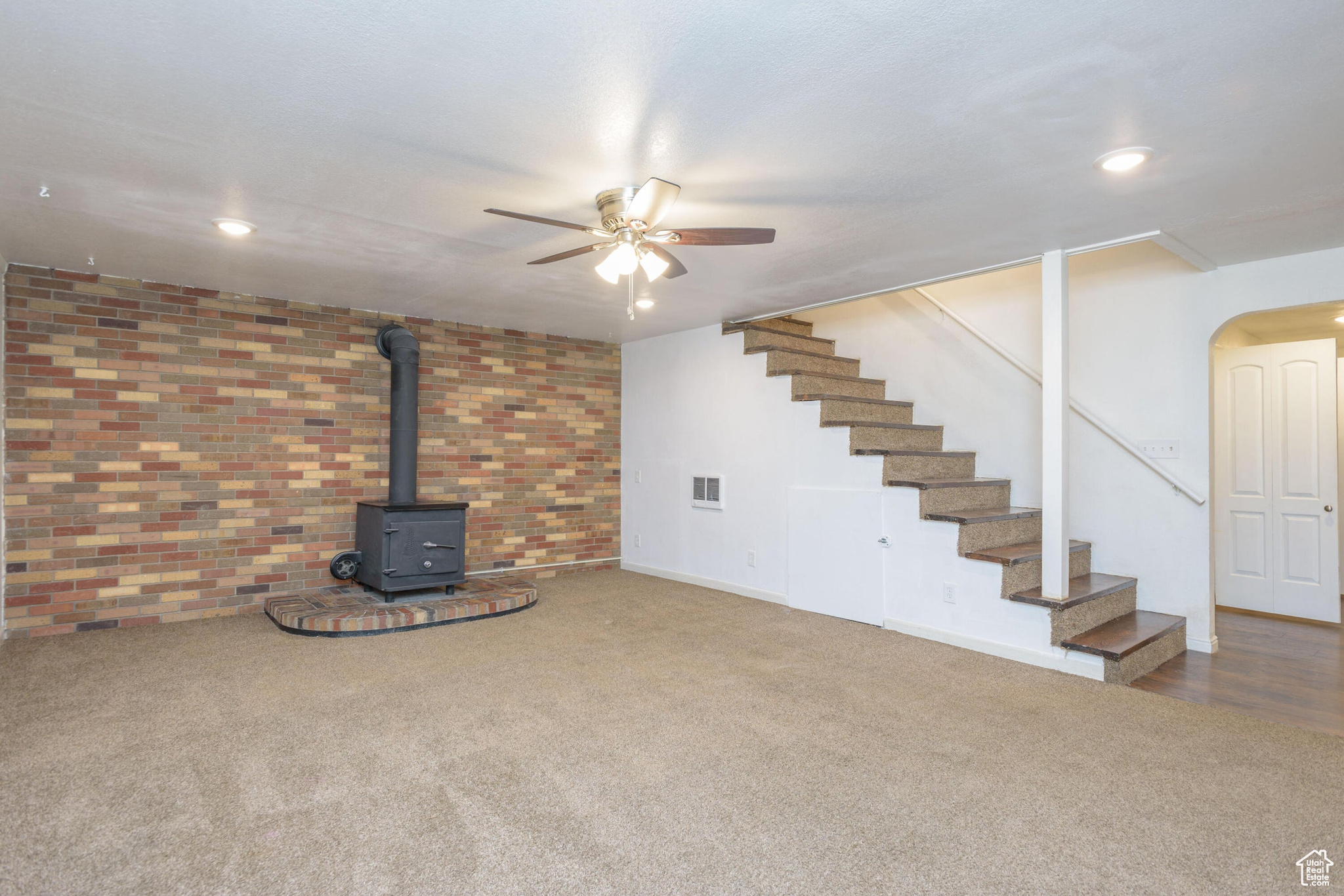 Basement with a wood stove, carpet flooring, brick wall, and ceiling fan