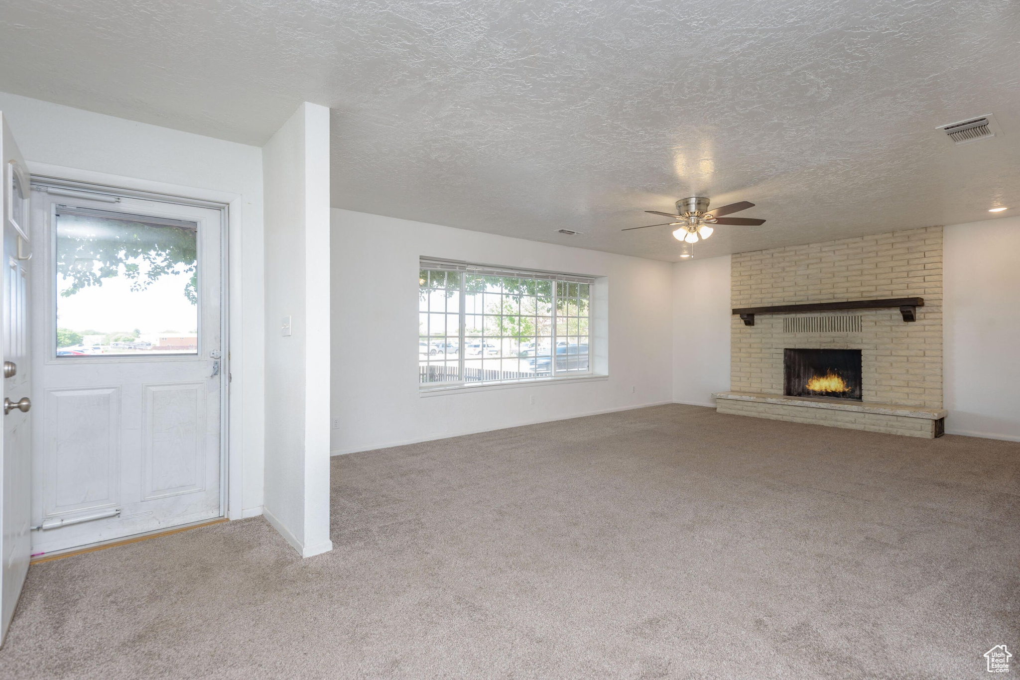 Unfurnished living room with a fireplace, a textured ceiling, light colored carpet, and ceiling fan