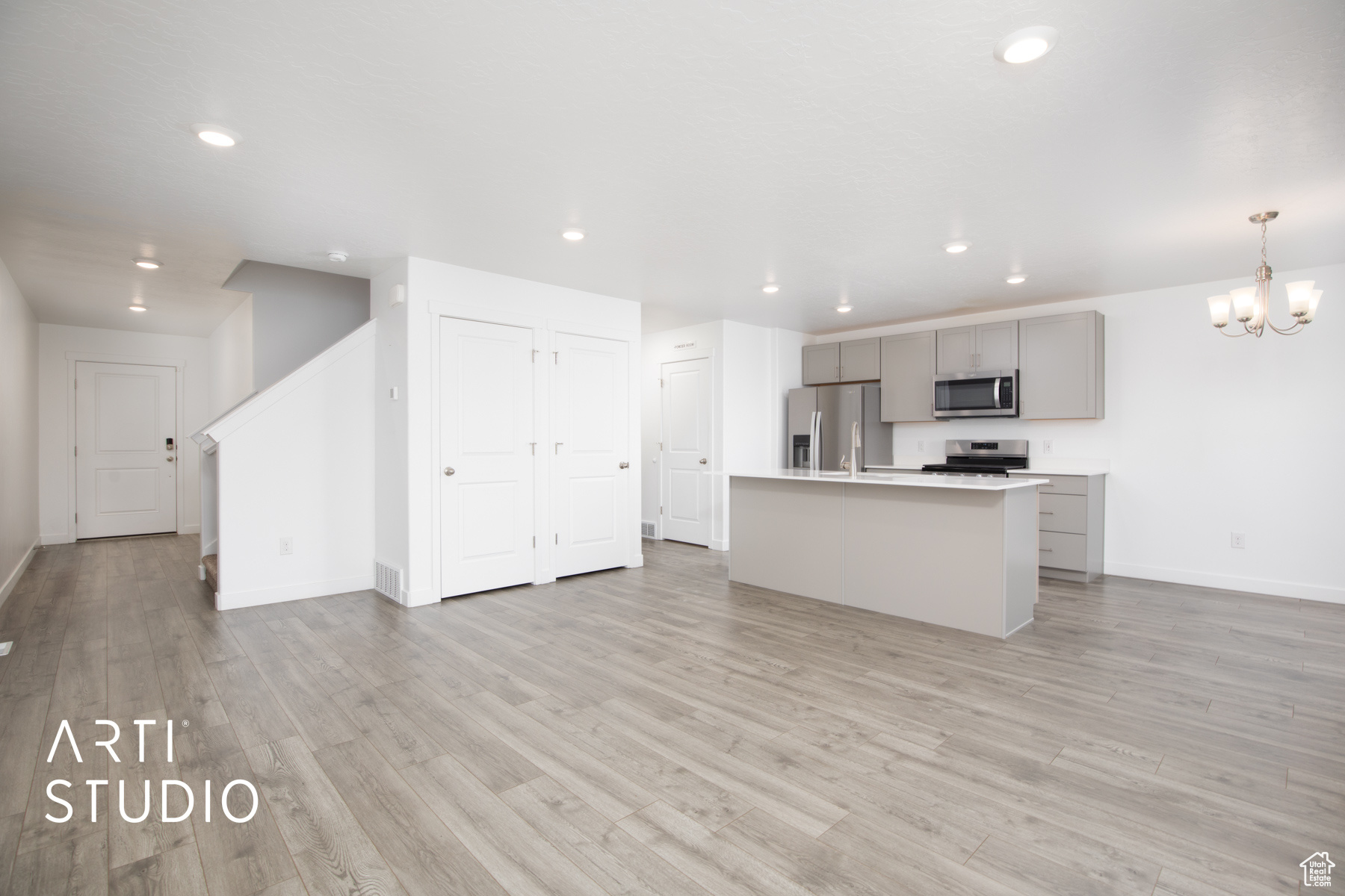 Kitchen with light hardwood / wood-style flooring, an island with sink, stainless steel appliances, decorative light fixtures, and gray cabinetry