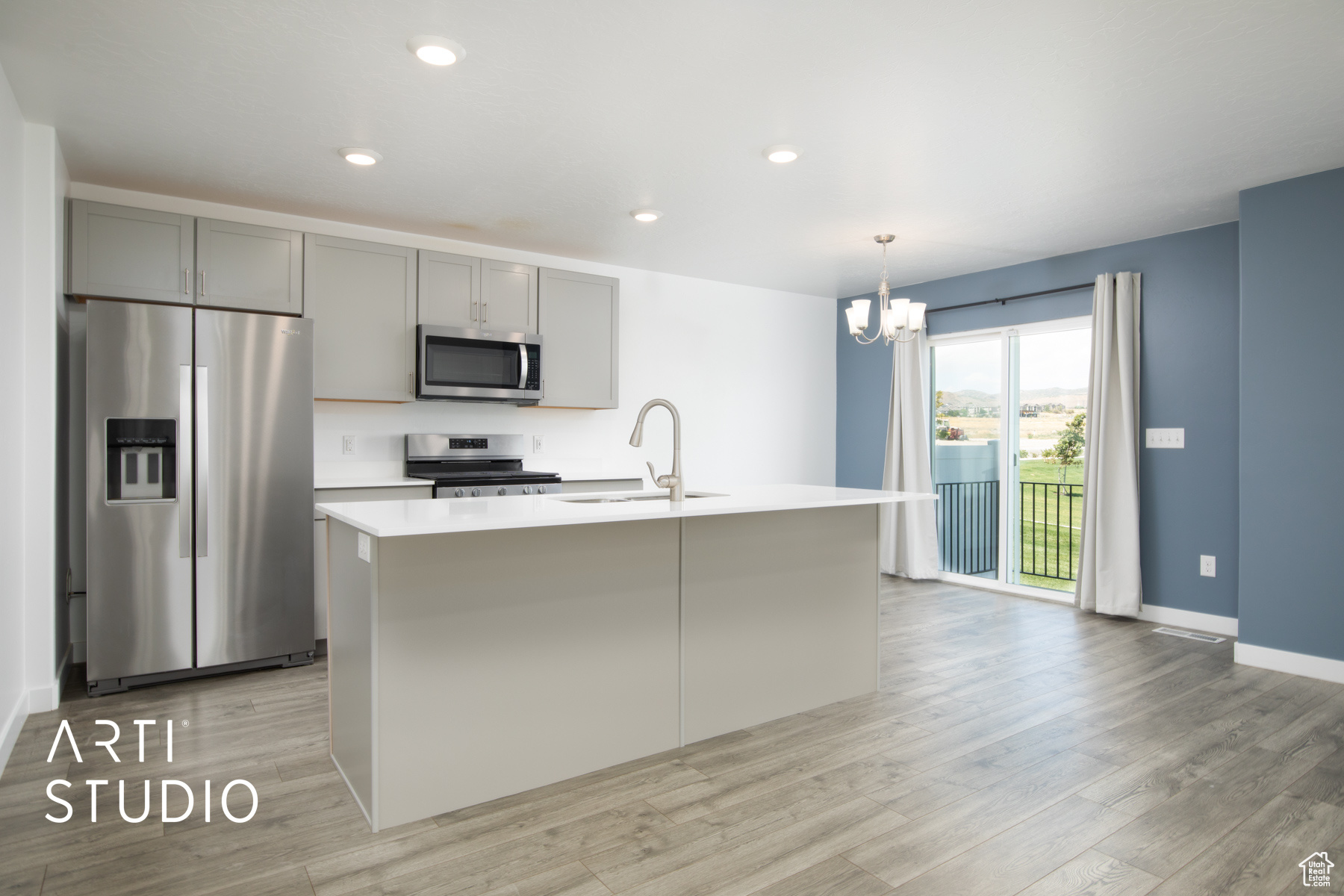 Kitchen featuring stainless steel appliances, gray cabinetry, a center island with sink, sink, and light wood-type flooring