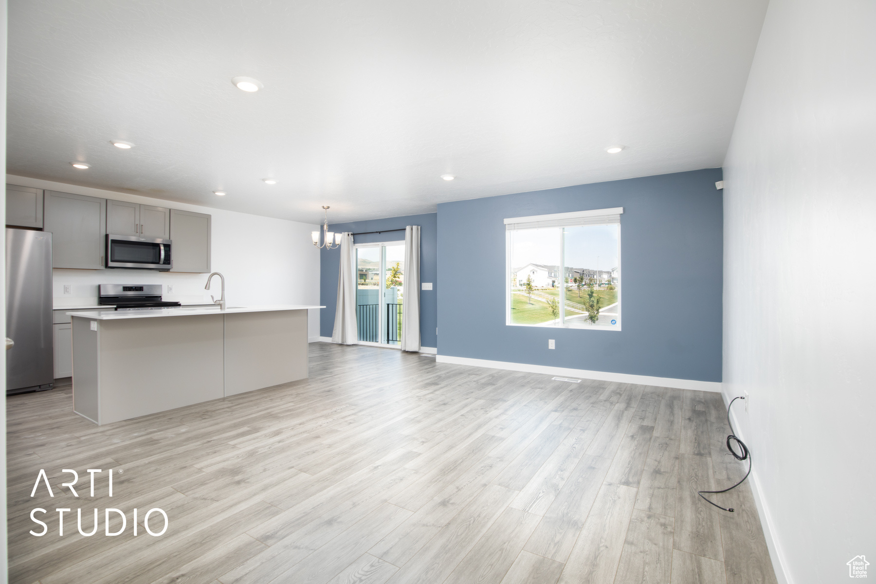 Kitchen with light wood-type flooring, an island with sink, gray cabinets, hanging light fixtures, and appliances with stainless steel finishes