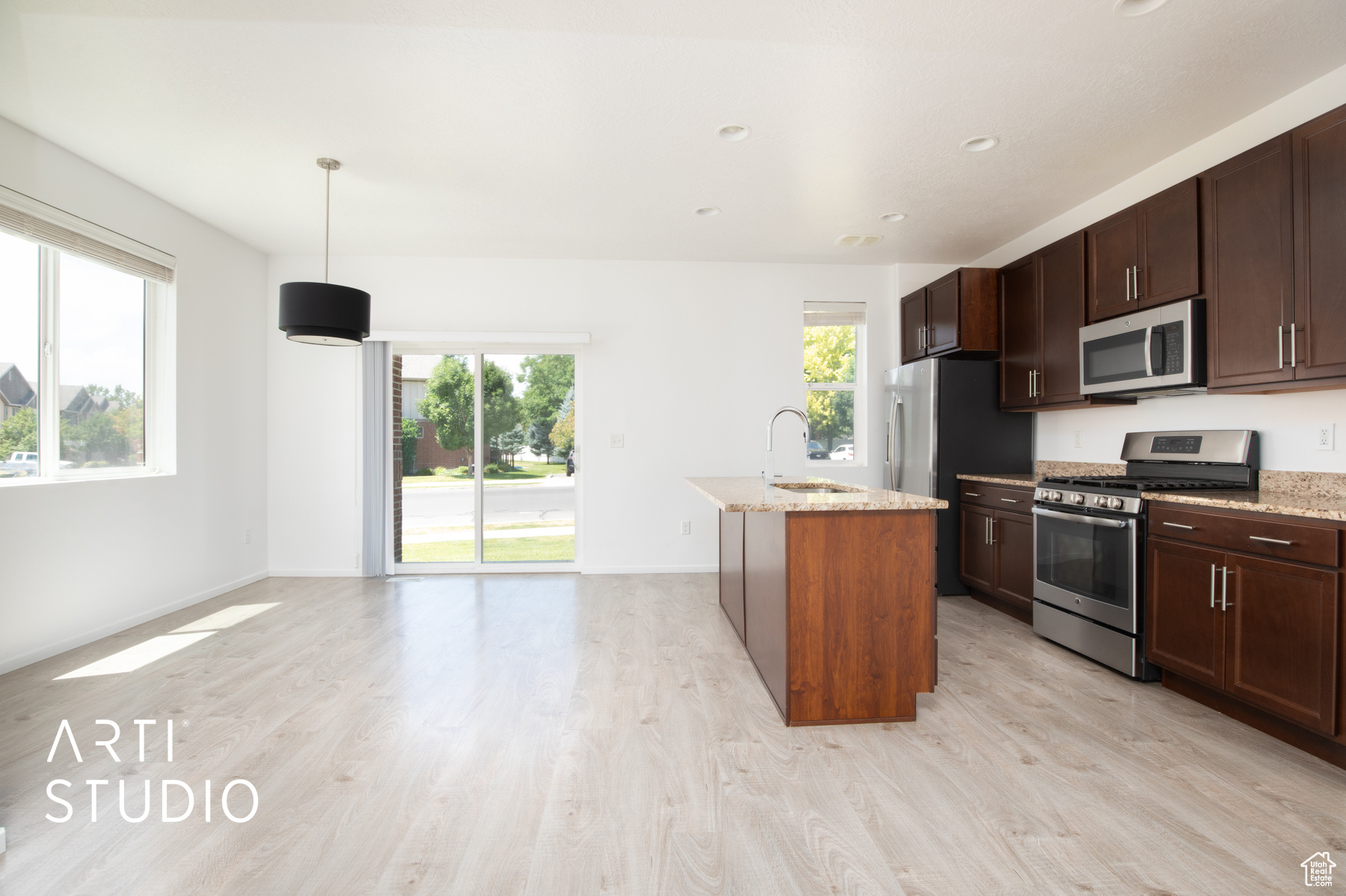 Kitchen featuring stainless steel appliances, light hardwood / wood-style floors, light stone countertops, decorative light fixtures, and sink