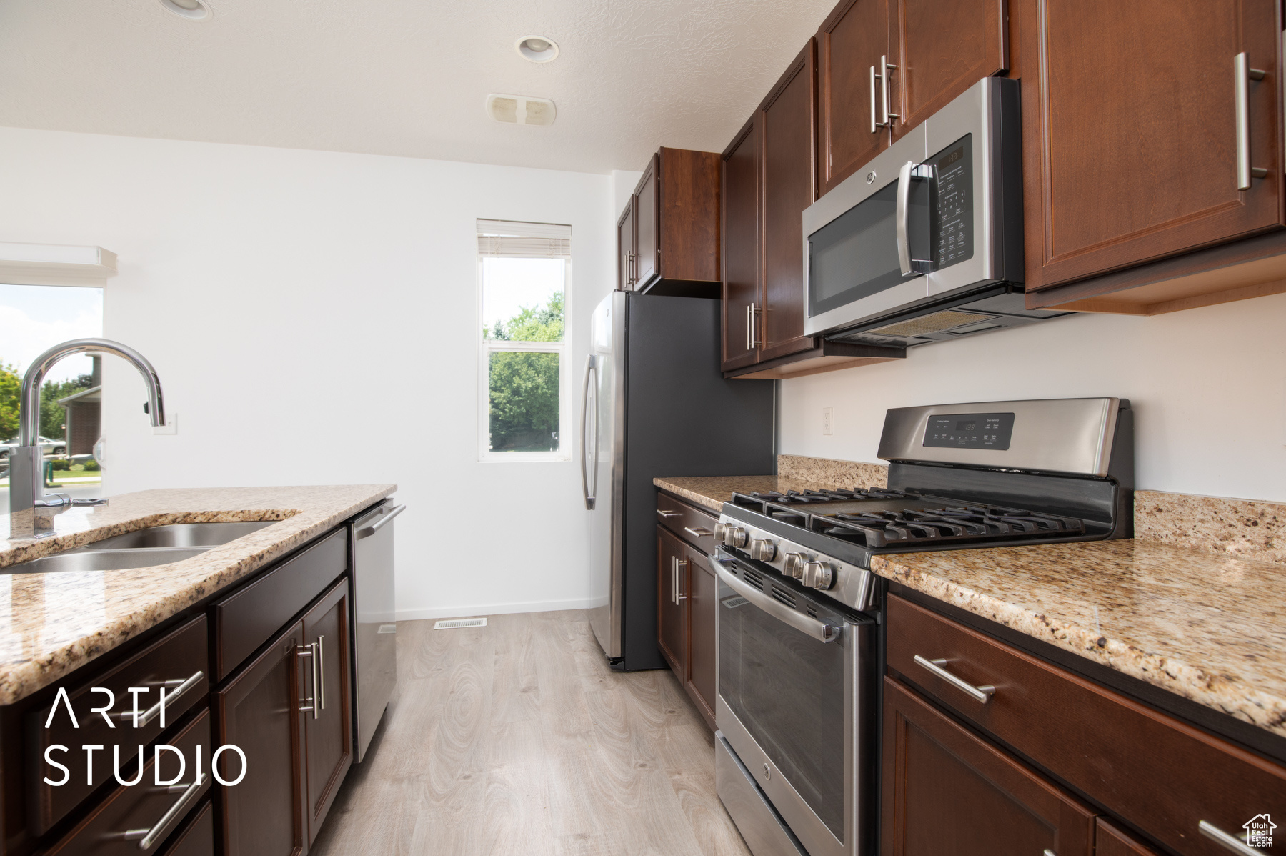 Kitchen featuring sink, light stone countertops, light wood-type flooring, and stainless steel appliances