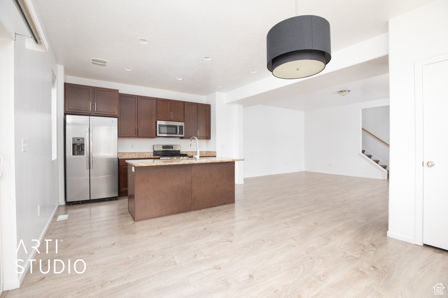 Kitchen with an island with sink, stainless steel appliances, light hardwood / wood-style floors, dark brown cabinetry, and sink