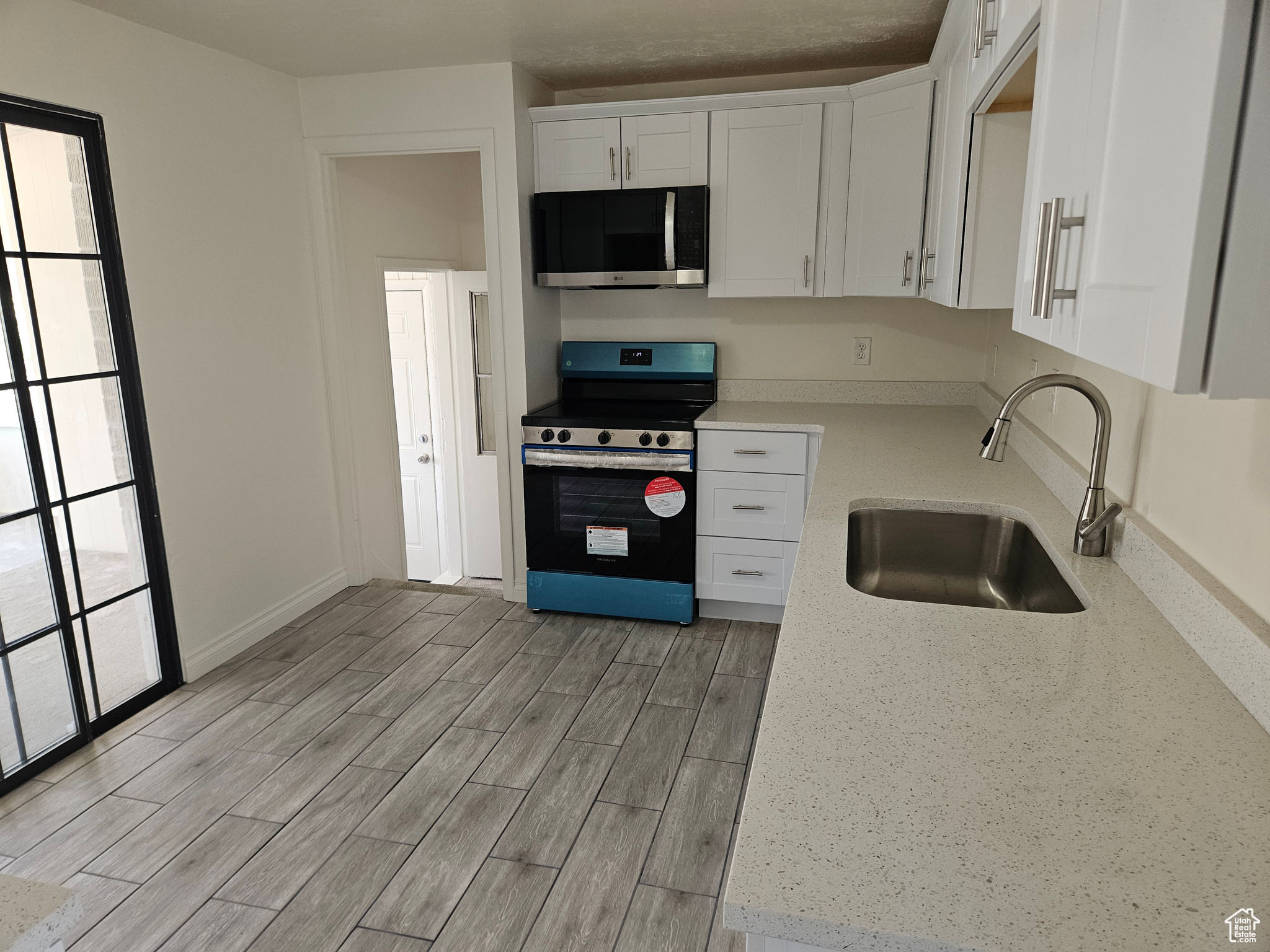 Kitchen featuring range with electric cooktop, white cabinets, sink, light hardwood / wood-style floors, and light stone countertops