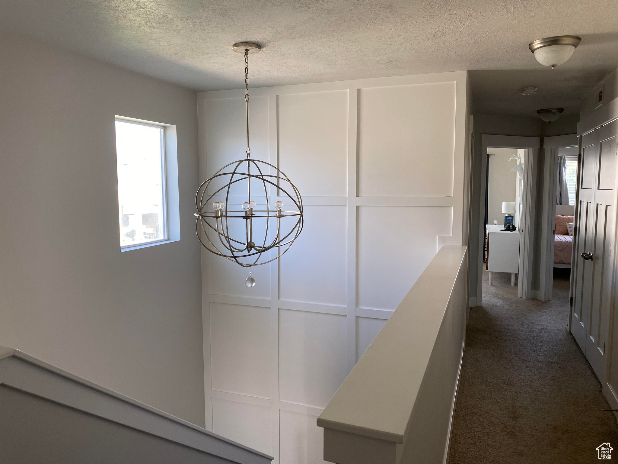 Hallway featuring a notable chandelier, dark colored carpet, and a textured ceiling