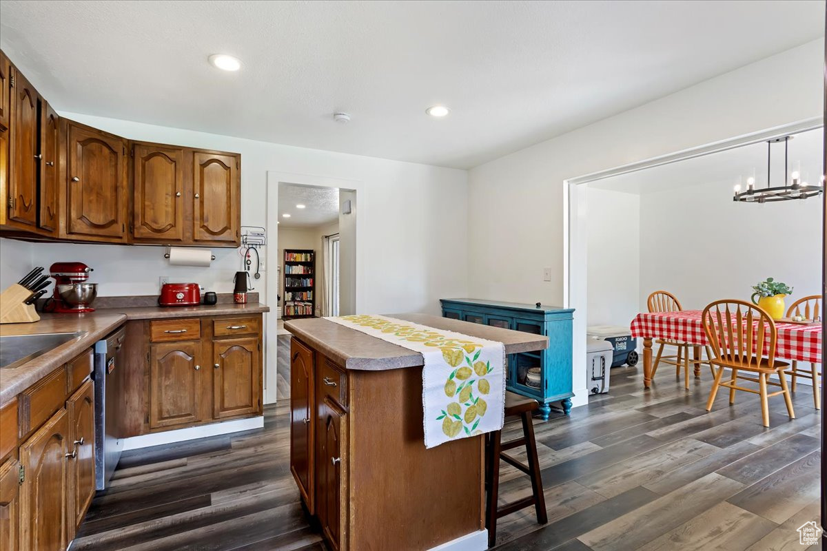 Kitchen with a notable chandelier, stainless steel dishwasher, pendant lighting, dark hardwood / wood-style floors, and a kitchen island