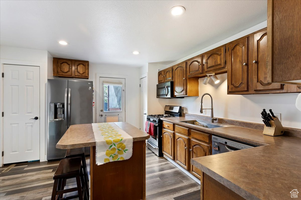 Kitchen with a breakfast bar, dark wood-type flooring, a kitchen island, appliances with stainless steel finishes, and sink