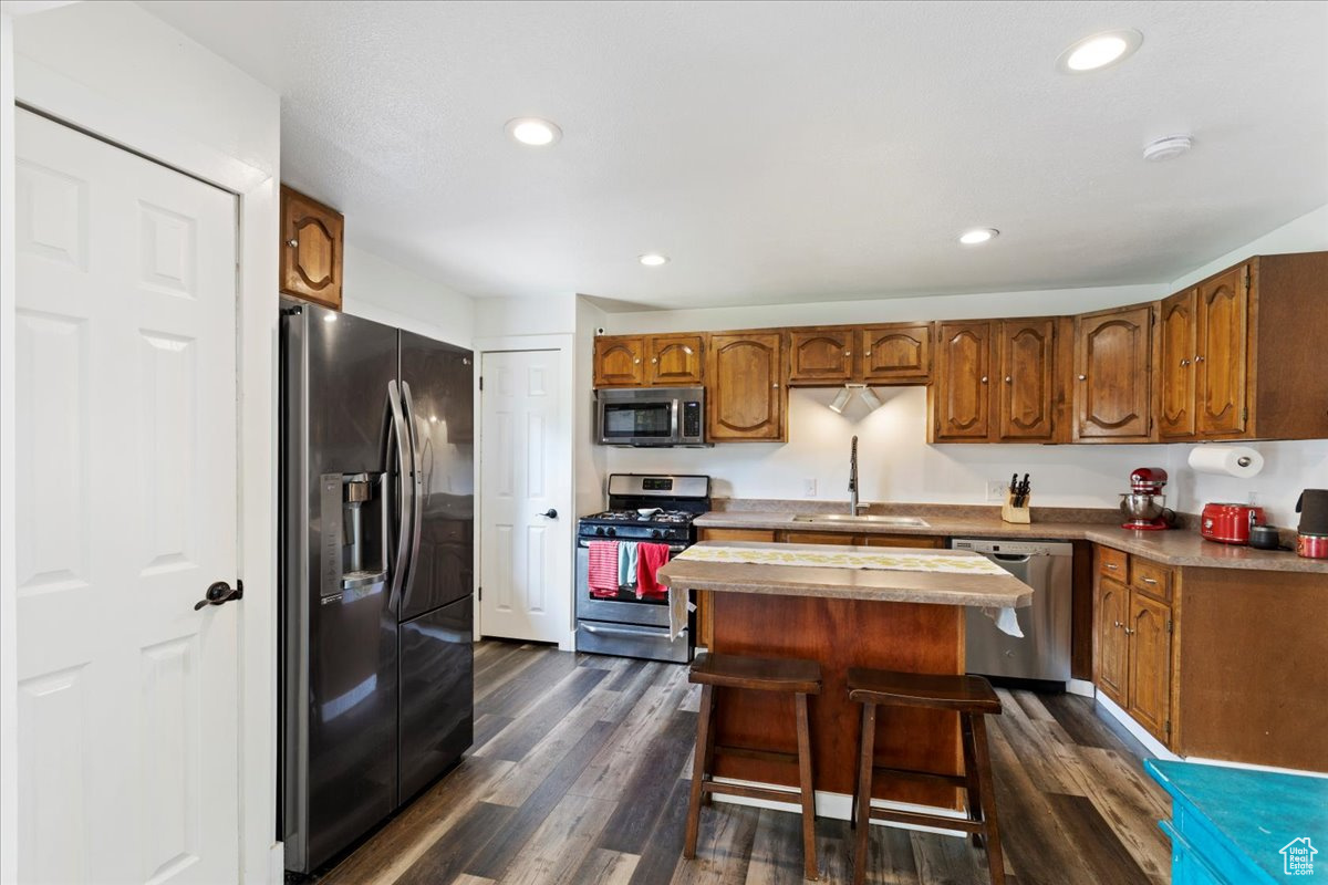 Kitchen featuring a breakfast bar area, a kitchen island, dark hardwood / wood-style floors, stainless steel appliances, and sink