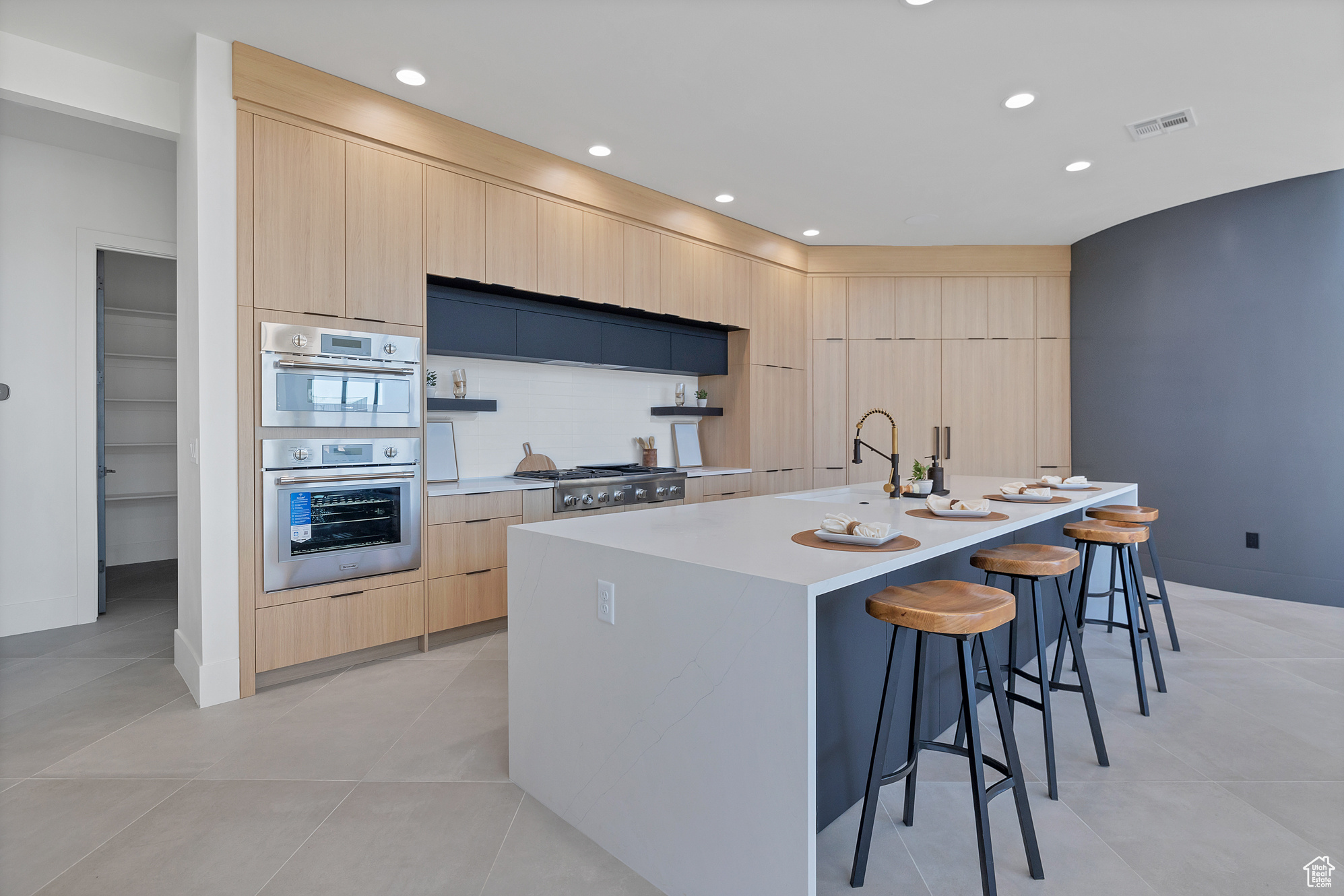 Kitchen featuring a kitchen bar, stainless steel appliances, light brown cabinetry, decorative backsplash, and a center island with sink