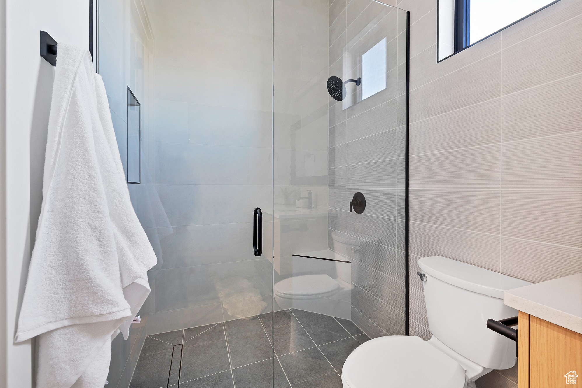 Bathroom with a shower with shower door, vanity, tile walls, and toilet