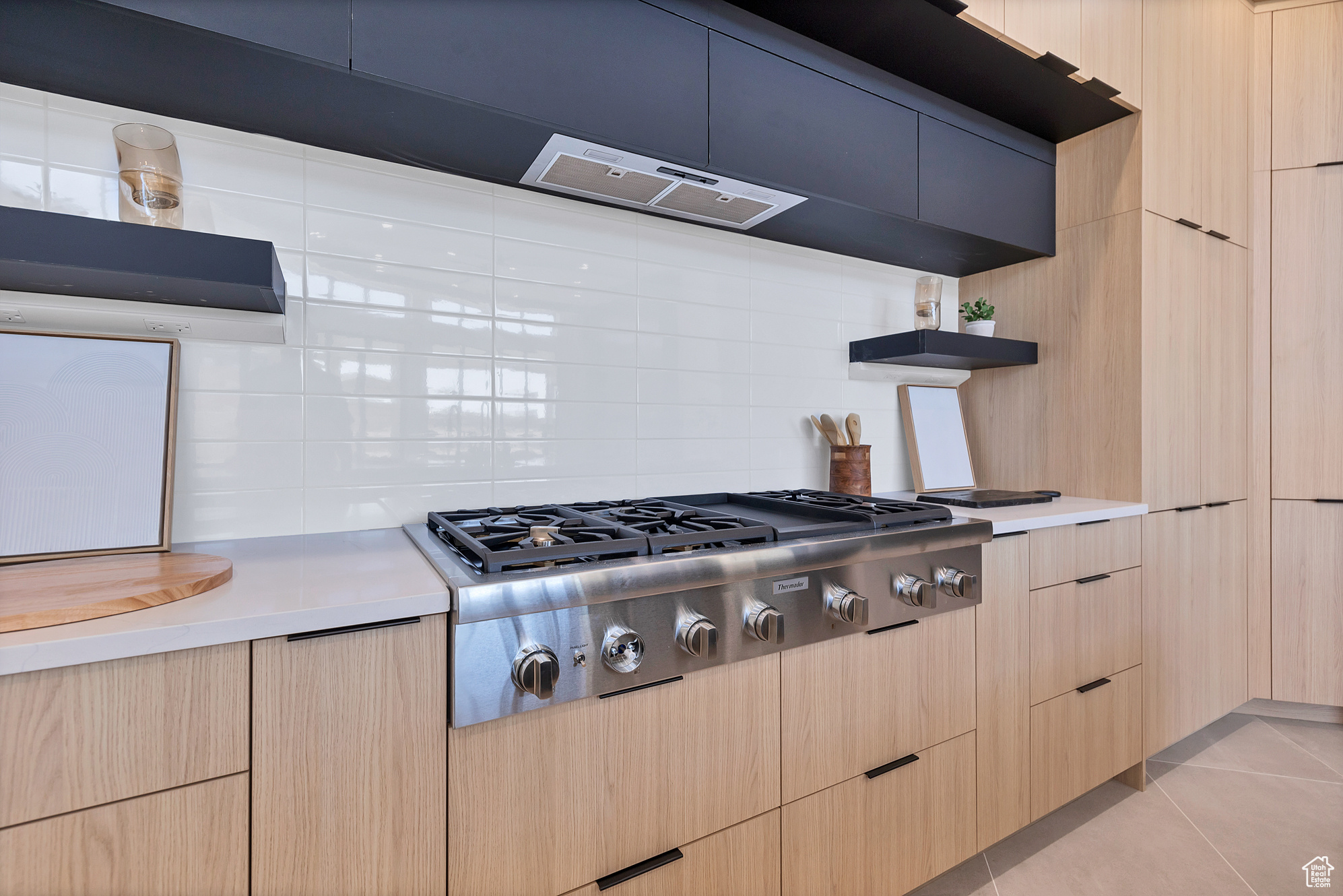 Kitchen featuring stainless steel gas stovetop, light tile patterned floors, backsplash, light brown cabinetry, and extractor fan