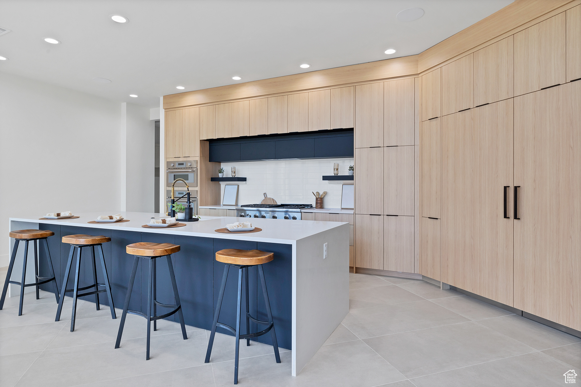 Kitchen featuring light tile patterned flooring, light brown cabinets, tasteful backsplash, and an island with sink