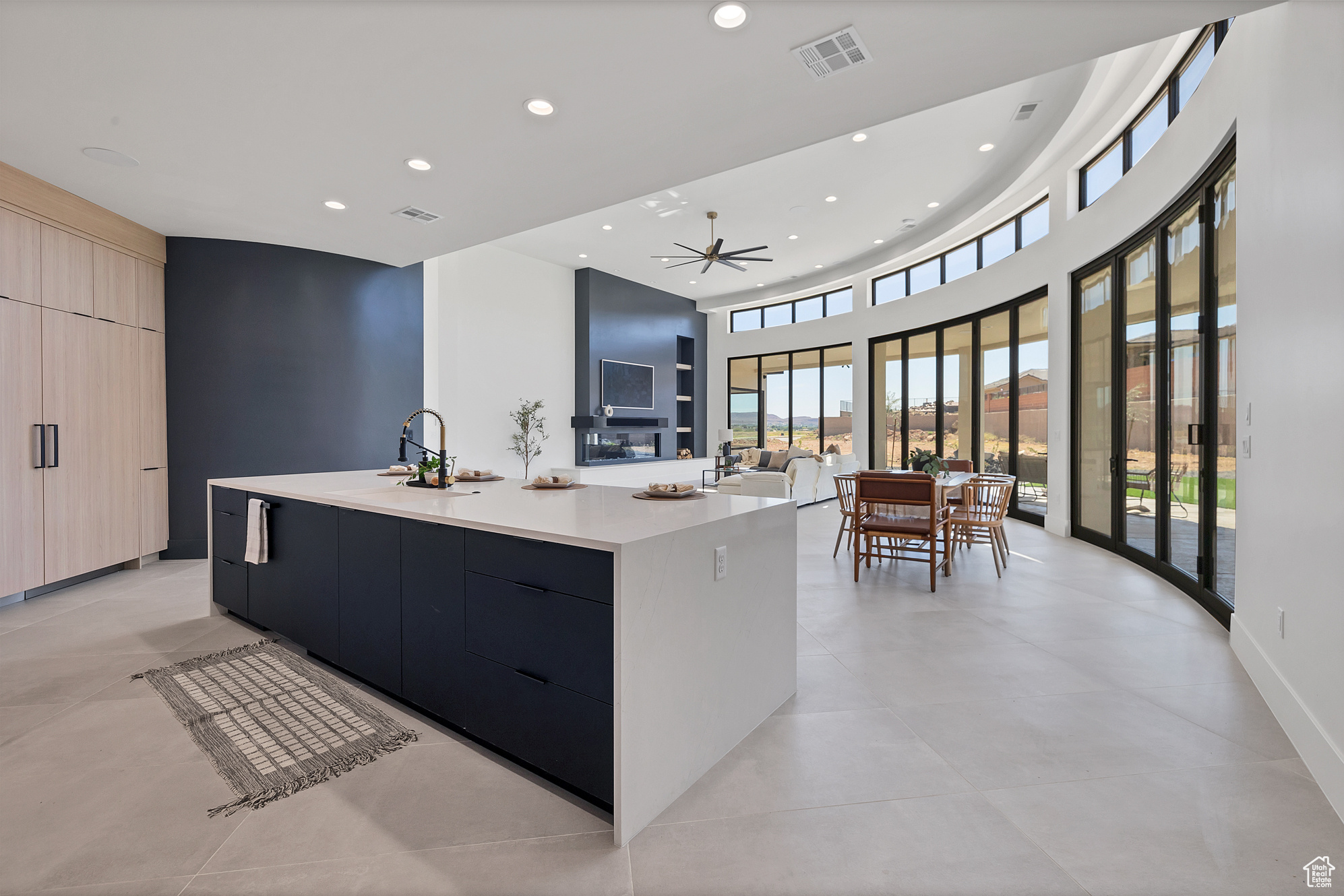 Kitchen featuring light brown cabinets, light tile patterned floors, ceiling fan, a towering ceiling, and a large island with sink