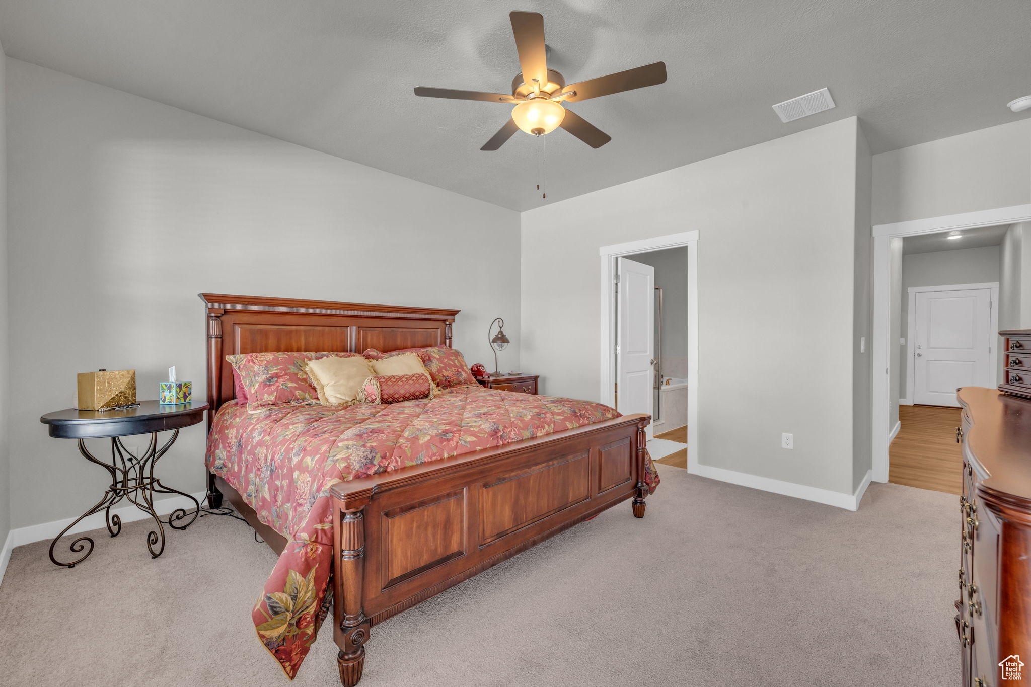 Bedroom with connected bathroom, light colored carpet, and ceiling fan