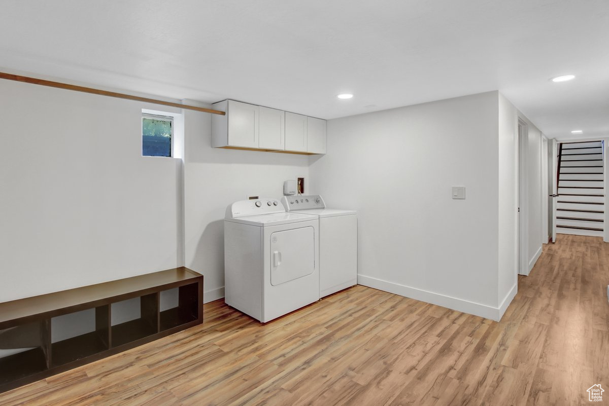 Clothes washing area featuring cabinets, light wood-type flooring, and washer and dryer