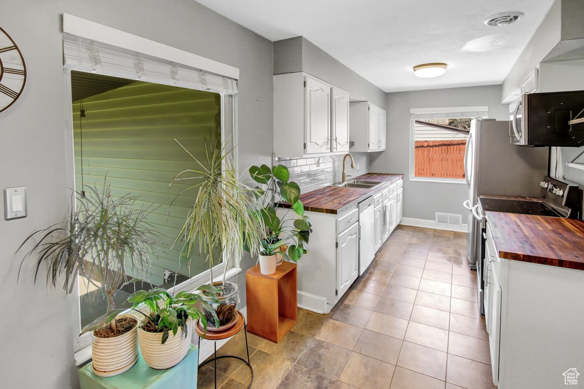 Kitchen with stainless steel appliances, wooden counters, sink, light tile patterned floors, and white cabinetry