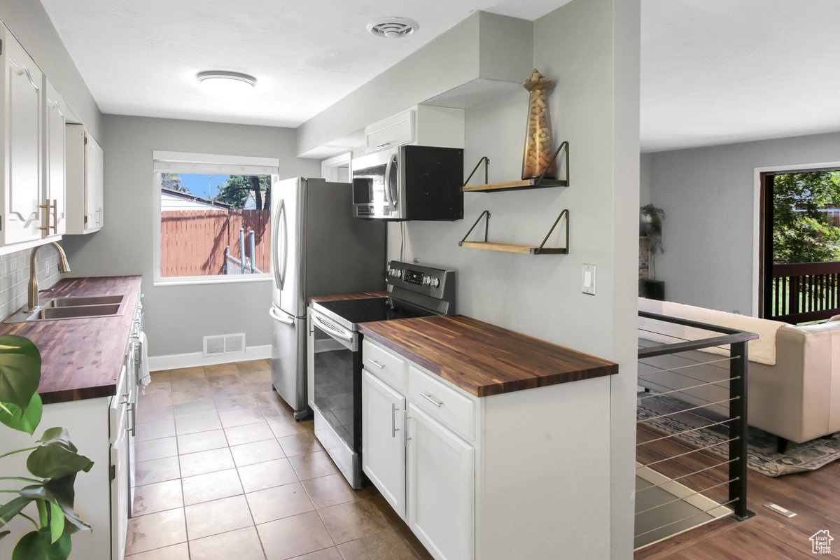 Kitchen featuring wooden counters, white cabinetry, appliances with stainless steel finishes, wood-type flooring, and sink