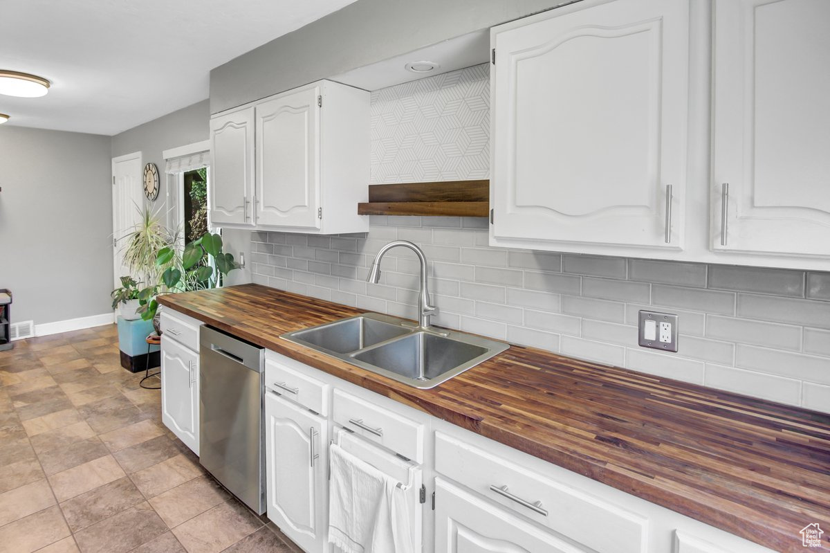 Kitchen featuring wooden counters, sink, stainless steel dishwasher, decorative backsplash, and white cabinetry