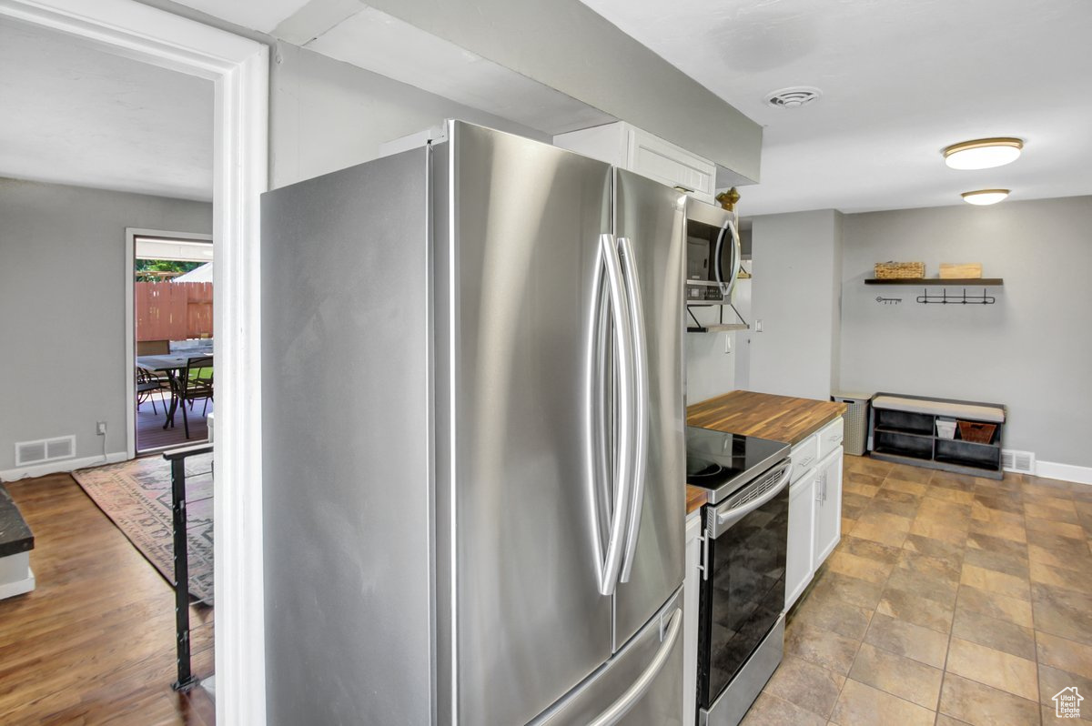 Kitchen with butcher block countertops, appliances with stainless steel finishes, white cabinets, and light tile patterned floors