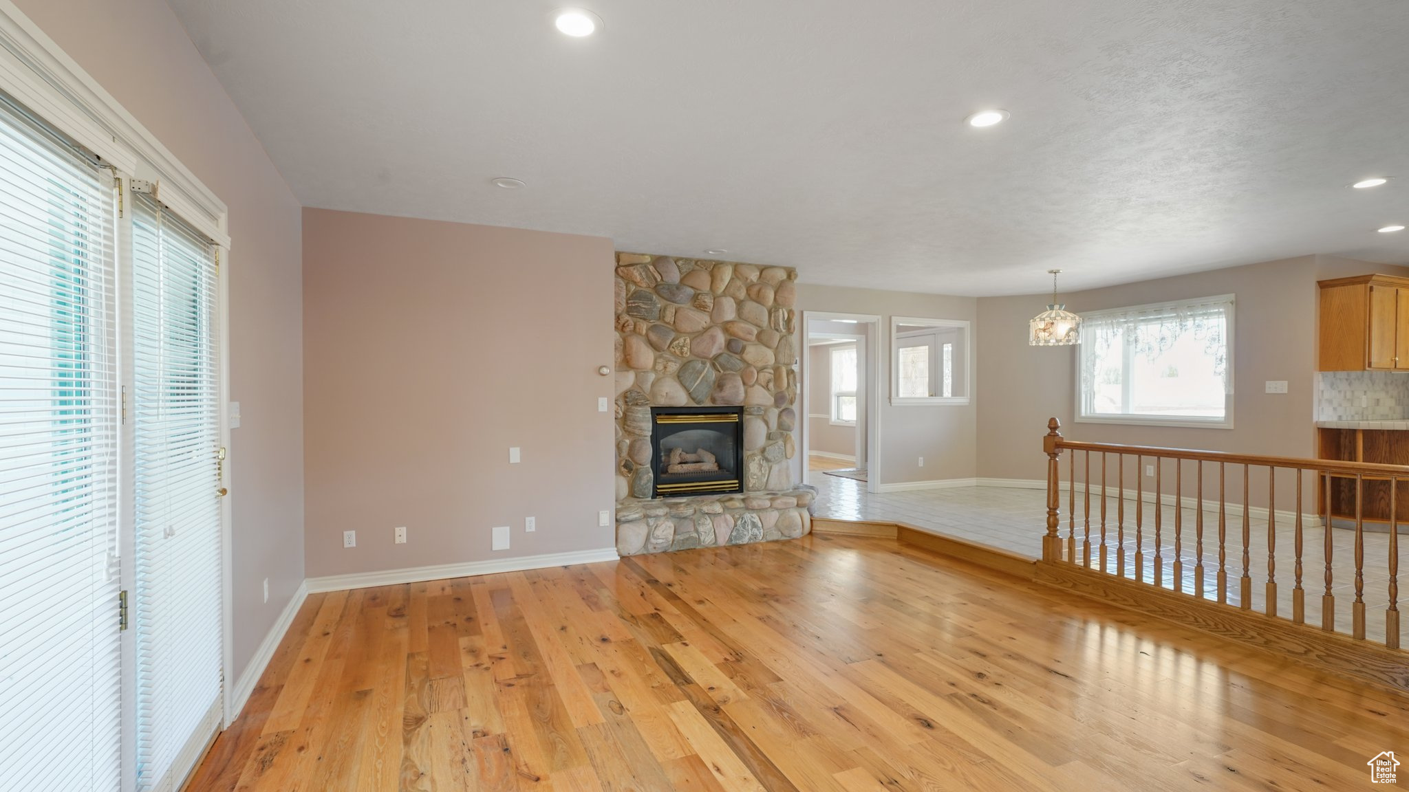 Unfurnished living room featuring a stone fireplace, a notable chandelier, and light hardwood / wood-style flooring