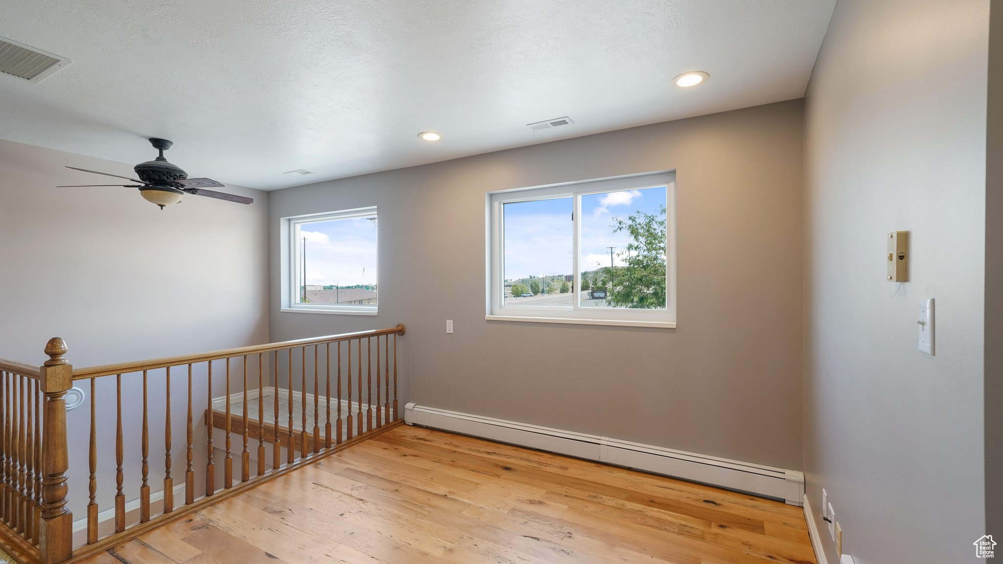 Empty room with a baseboard radiator, ceiling fan, and light hardwood / wood-style floors