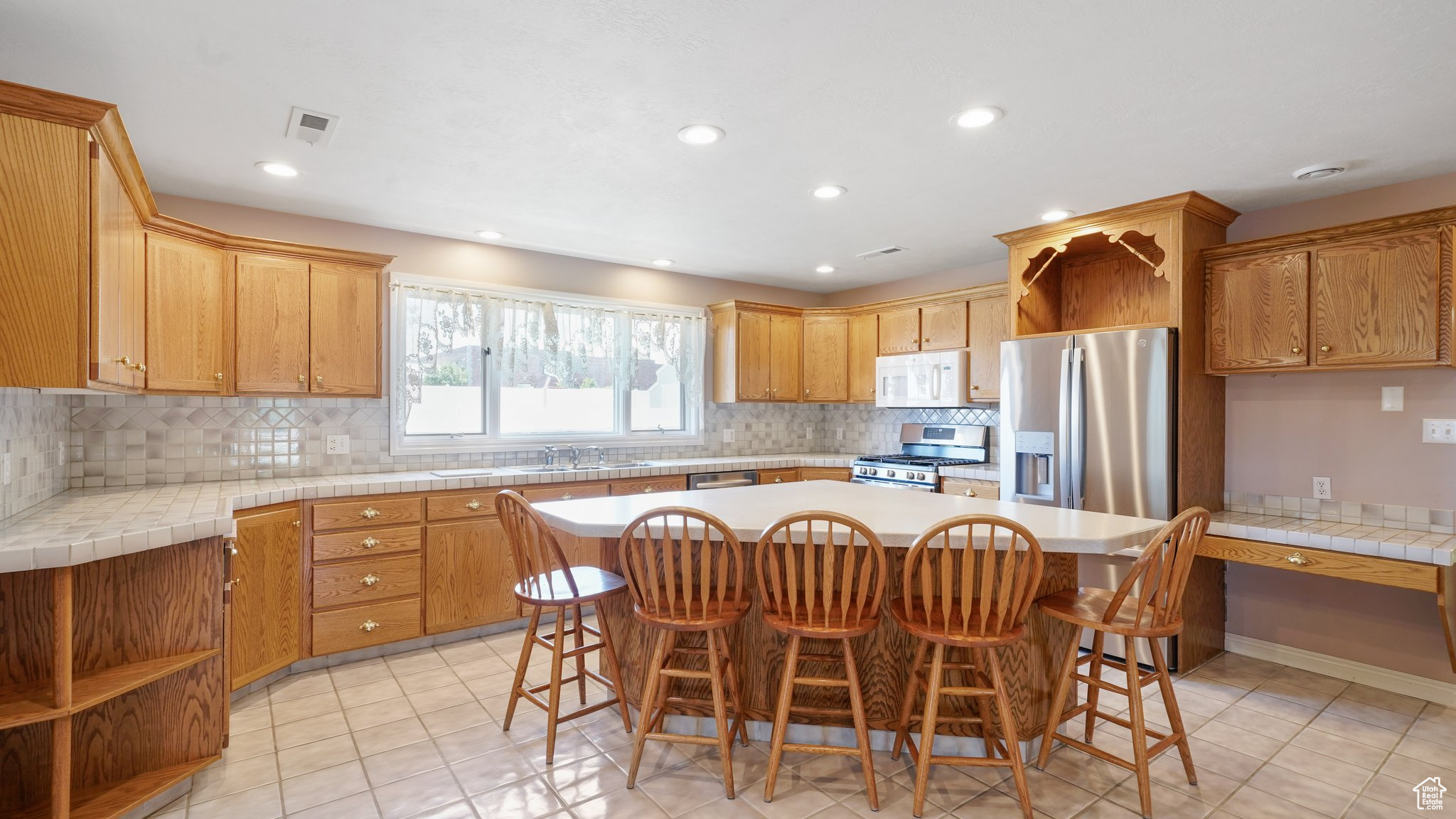 Kitchen featuring light tile patterned floors, a kitchen island, appliances with stainless steel finishes, decorative backsplash, and a kitchen bar