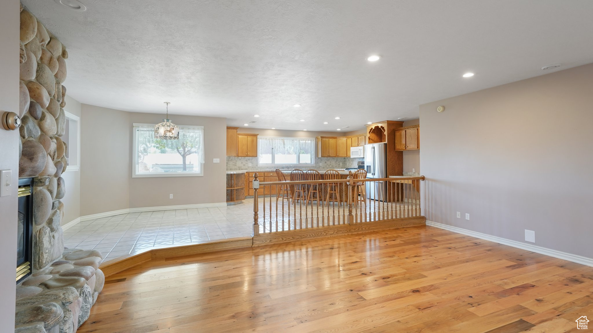 Unfurnished living room featuring an inviting chandelier, a stone fireplace, a textured ceiling, and light hardwood / wood-style floors