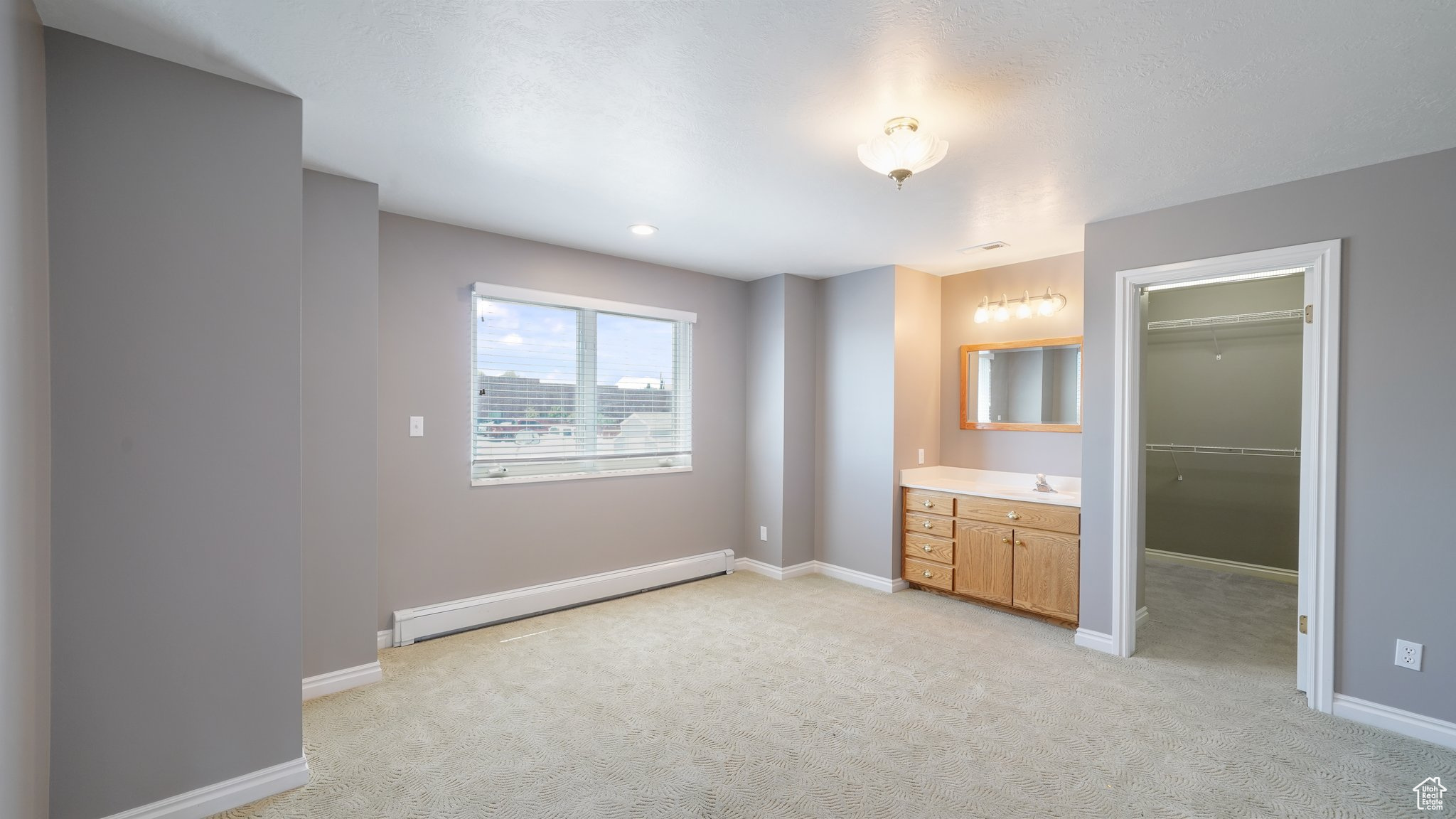 Unfurnished bedroom with vanity & sink, a spacious closet, light colored carpet, a baseboard radiator, and a closet