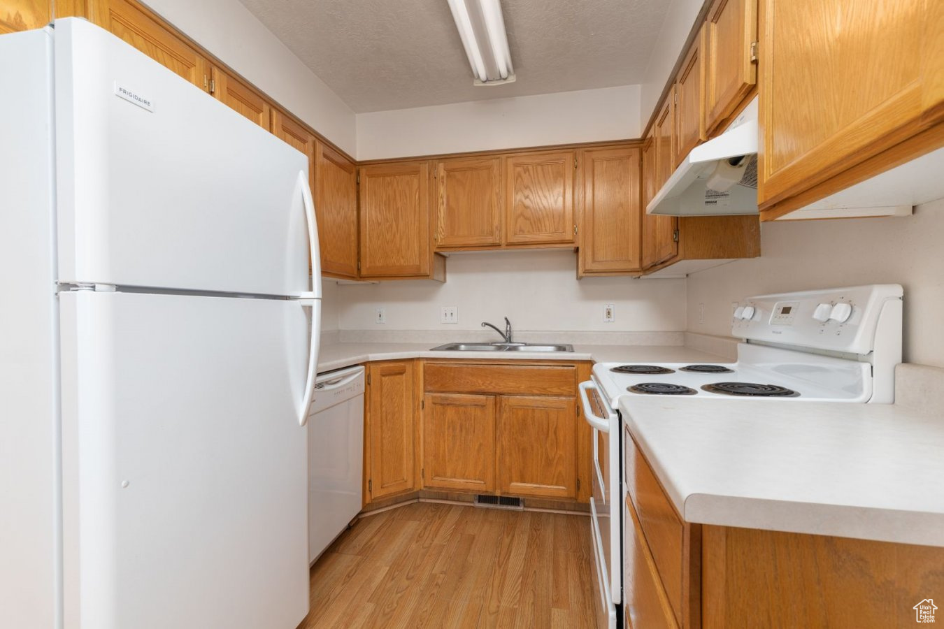 Kitchen featuring sink, light hardwood / wood-style flooring, white appliances, and wall chimney exhaust hood