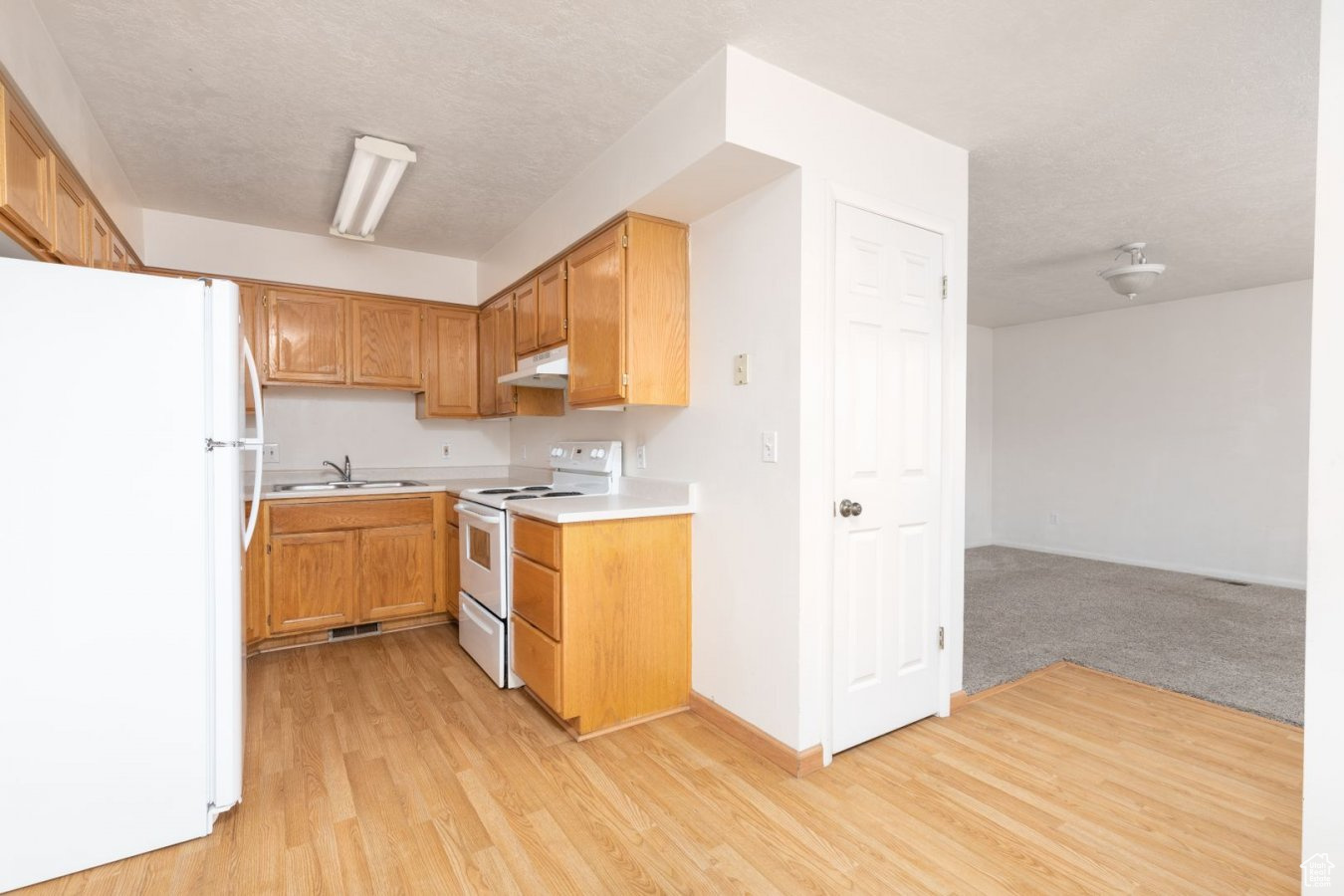 Kitchen featuring sink, light colored carpet, and white appliances