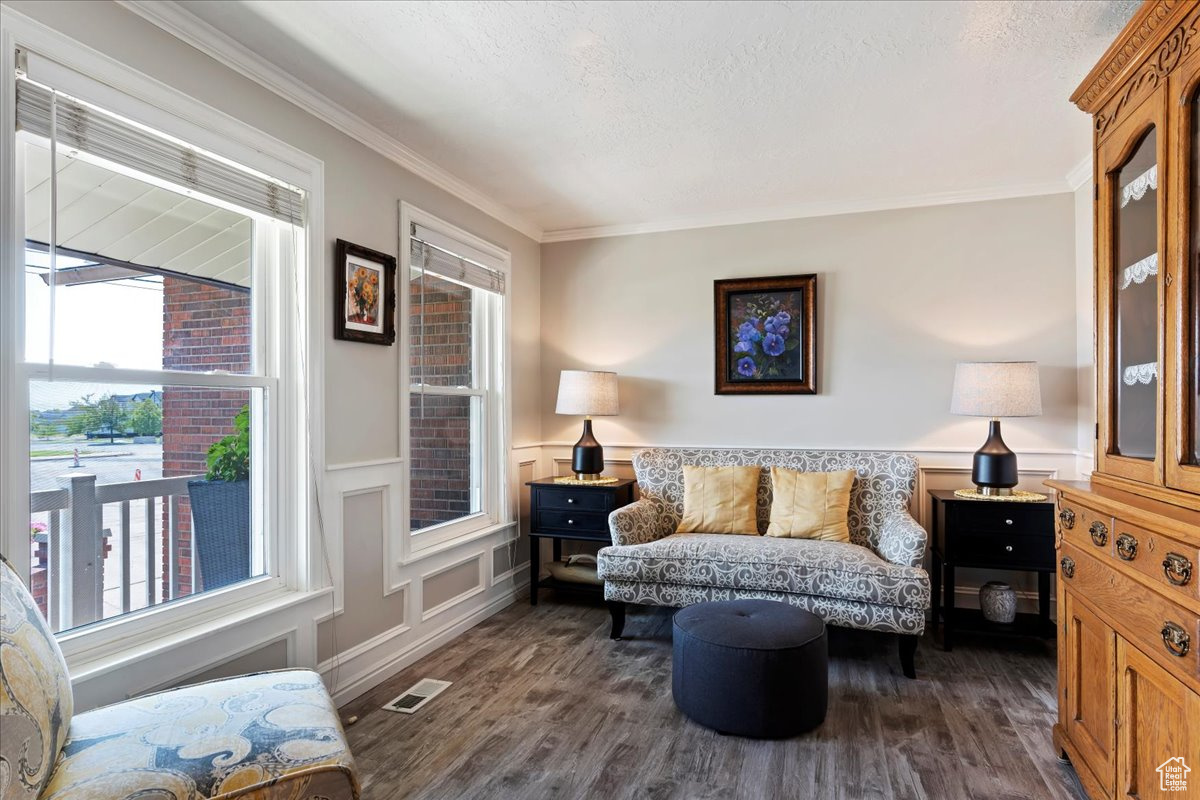 Living room with dark wood-type flooring, crown molding, and a healthy amount of sunlight