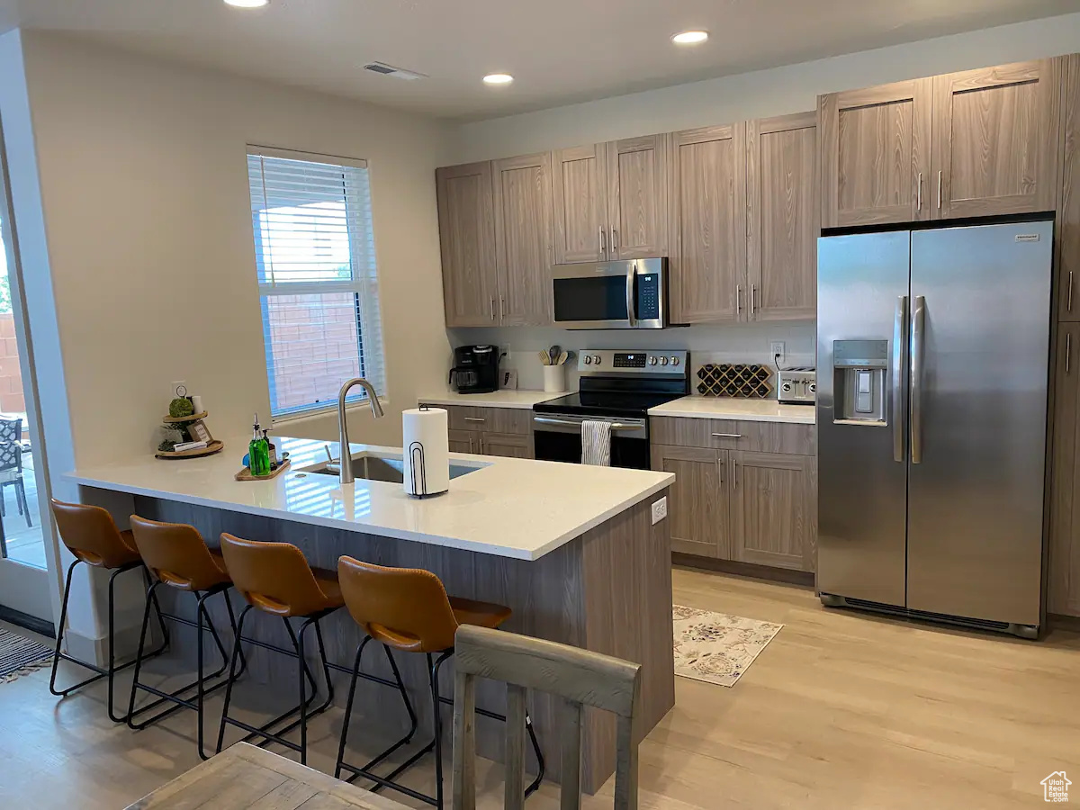 Kitchen with stainless steel appliances, light hardwood / wood-style floors, a breakfast bar area, and sink