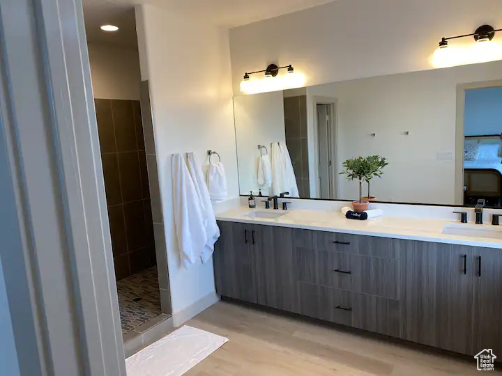 Bathroom with a tile shower, wood-type flooring, and dual bowl vanity