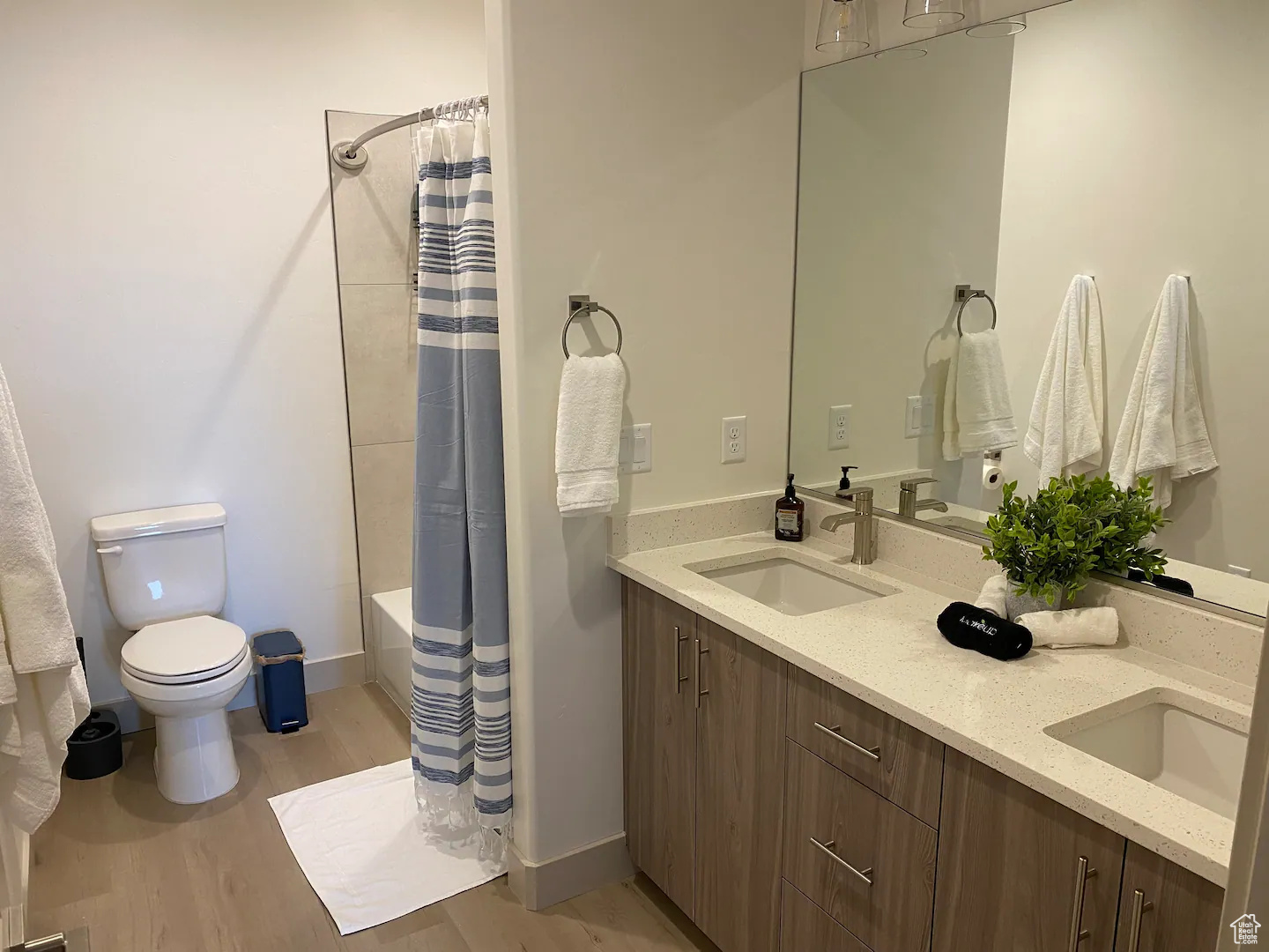 Full bathroom with double vanity, shower / bath combo, toilet, and hardwood / wood-style floors