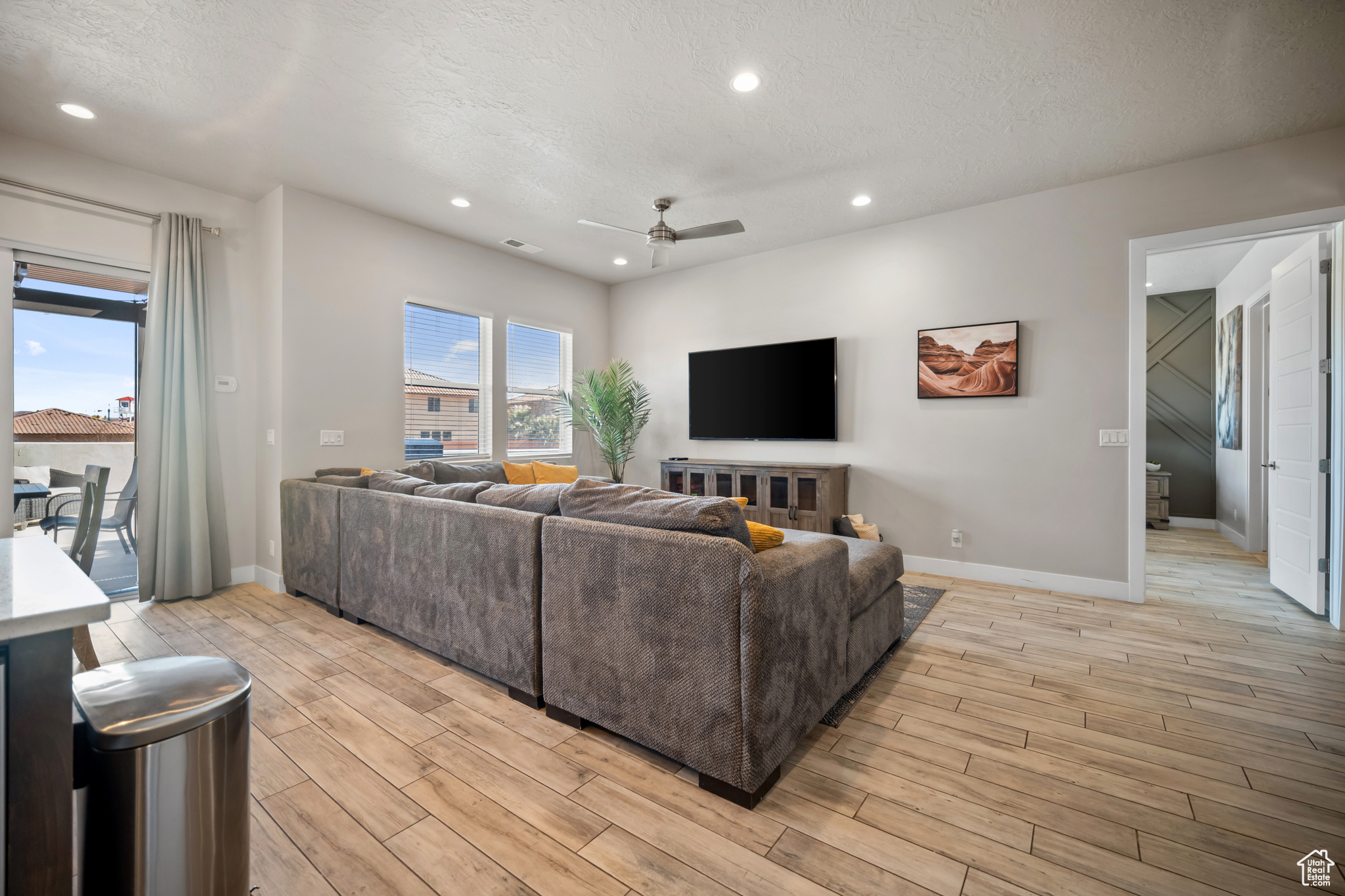 Living room with a textured ceiling, ceiling fan, and light hardwood / wood-style floors