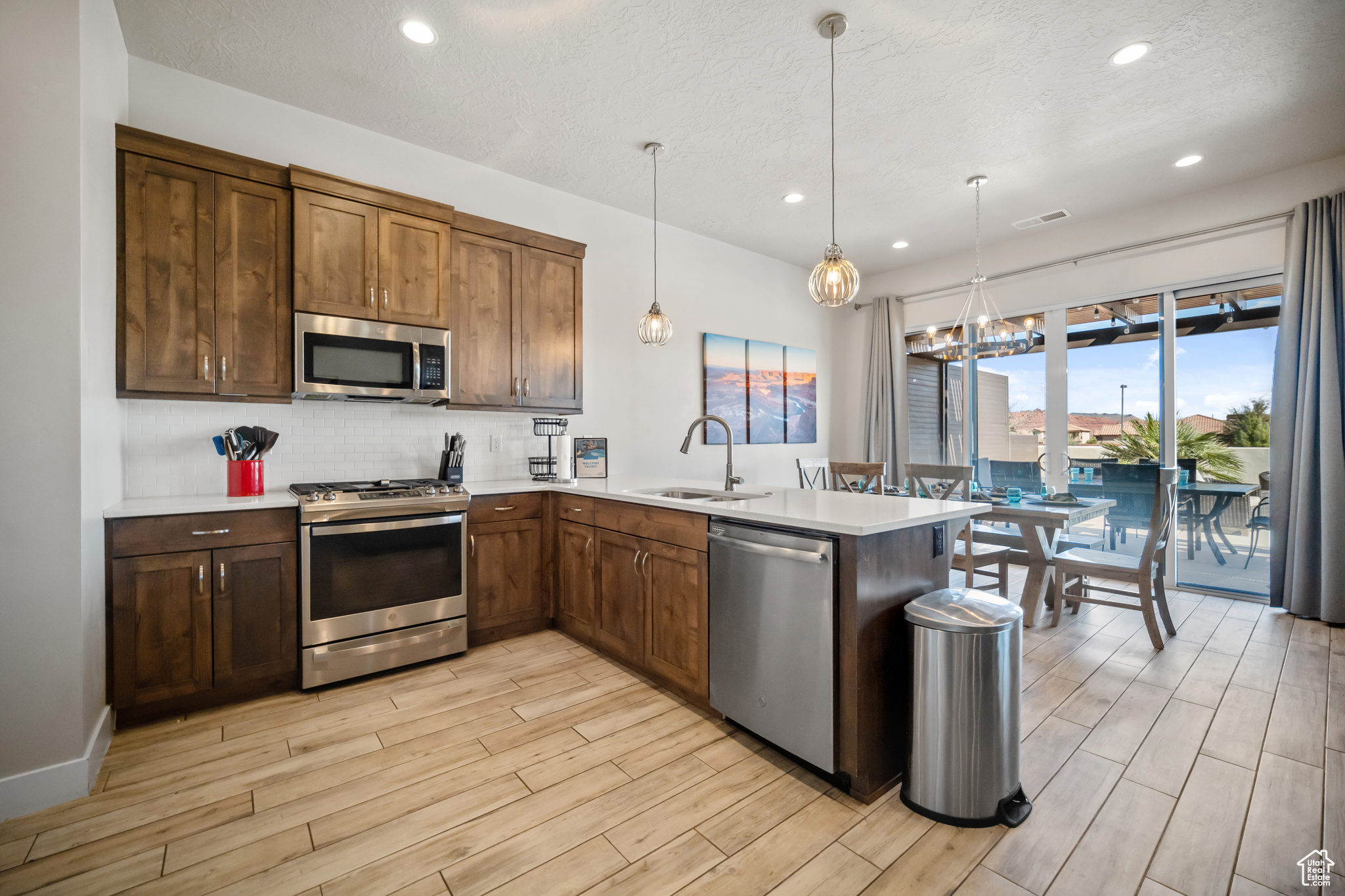 Kitchen with appliances with stainless steel finishes, light hardwood / wood-style flooring, tasteful backsplash, sink, and pendant lighting